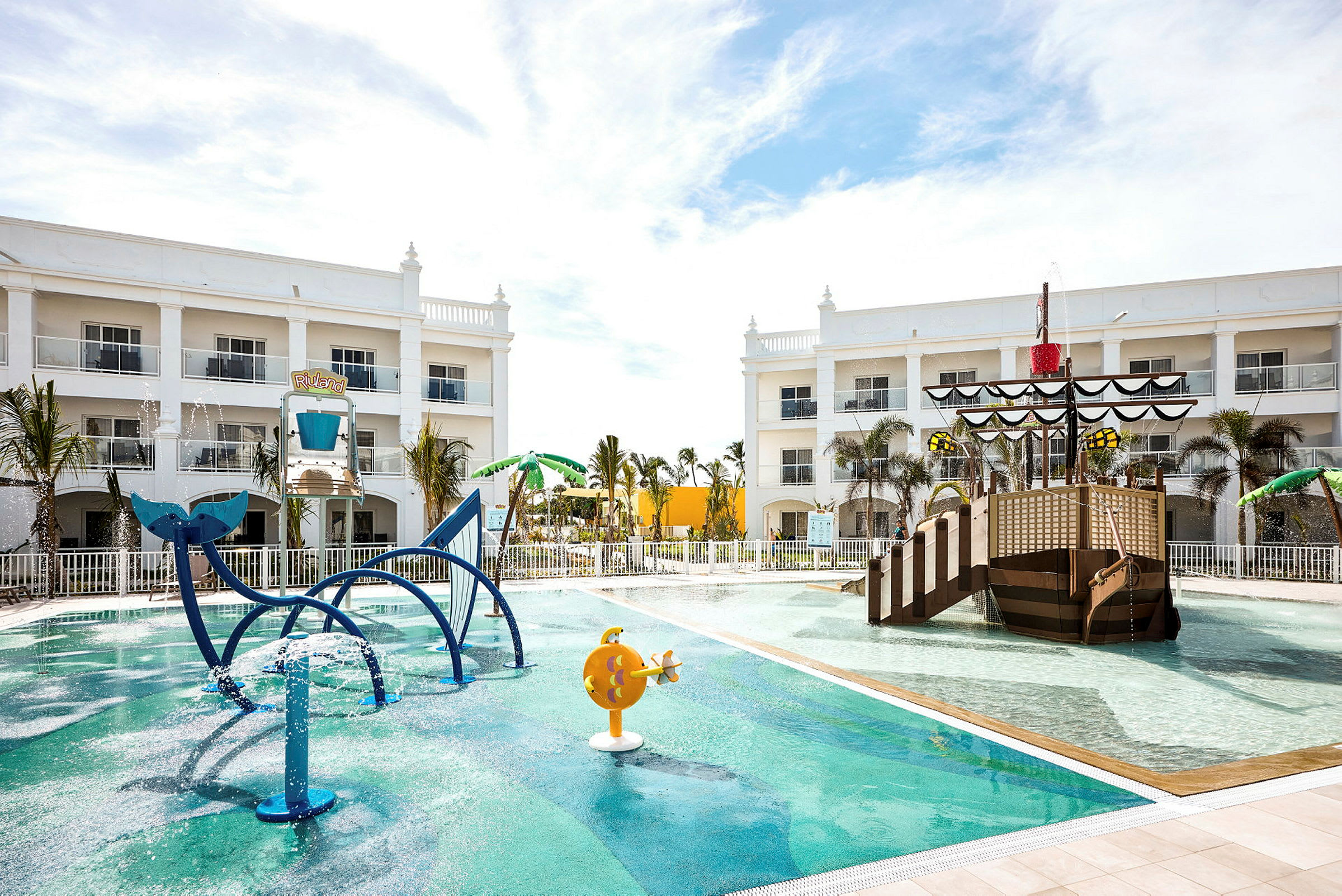 Barnpool med lekattraktioner och ett piratskepp på ett hotellområde. (AI-genererad text)