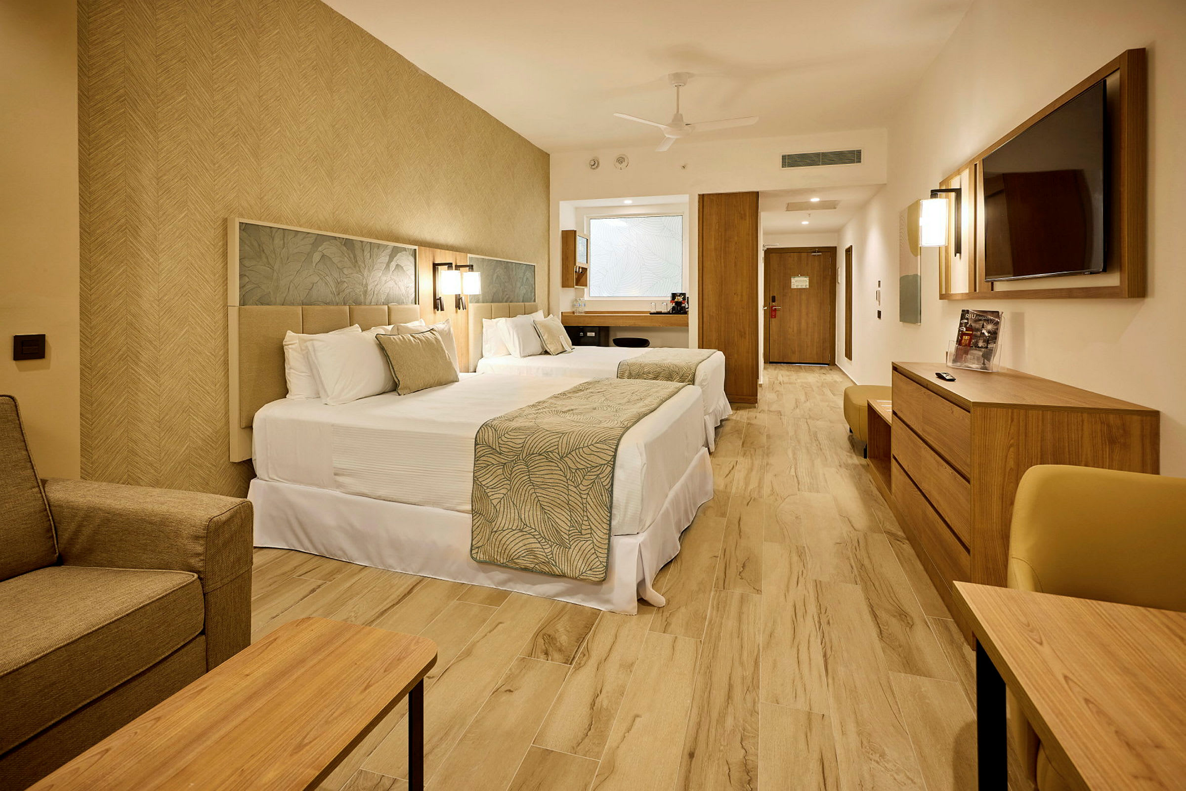 Ett hotellrum med två dubbelsängar, en tv på väggen, och ljusa trämöbler. (AI-genererad text)