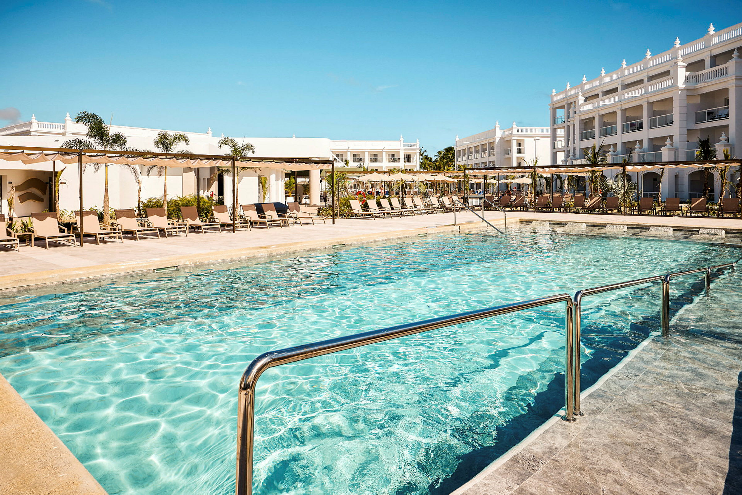 Utomhuspool med solsängar och hotellbyggnader i bakgrunden. (AI-genererad text)