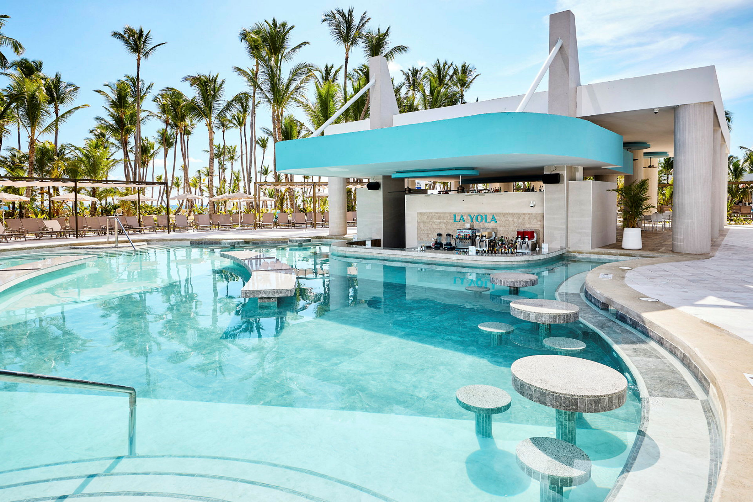 Pool med bar och sittplatser i vattnet, omgiven av solstolar och palmer. (AI-genererad text)