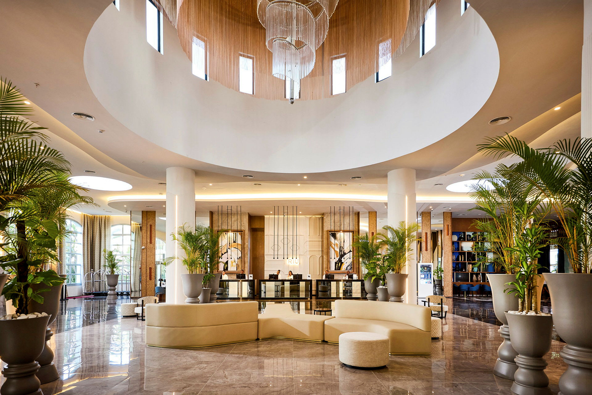 Lobby med cirkulära takfönster, ljuskrona, palmer och moderna möbler. (AI-genererad text)