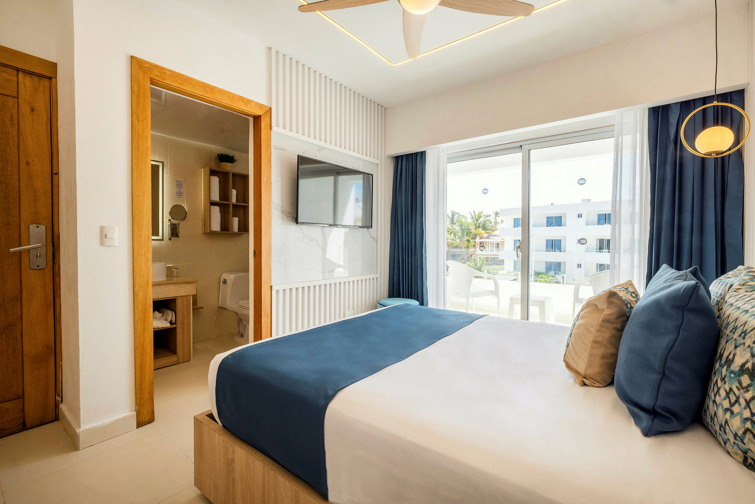 Ett modernt hotellrum med en dubbelsäng, badrum i anslutning till vänster och fönster mot en balkong. (AI-genererad text)
