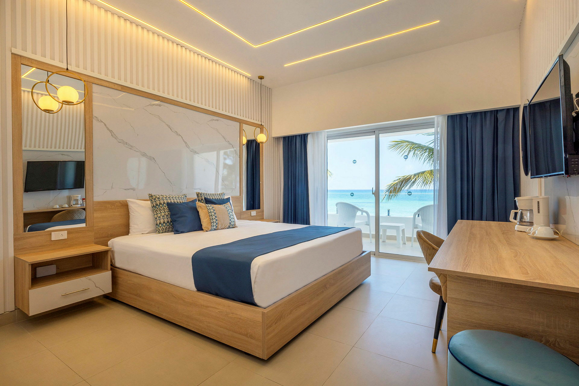 Ett stilrent hotellrum med en stor säng, träinredning och utsikt mot havet genom glasdörrar. (AI-genererad text)