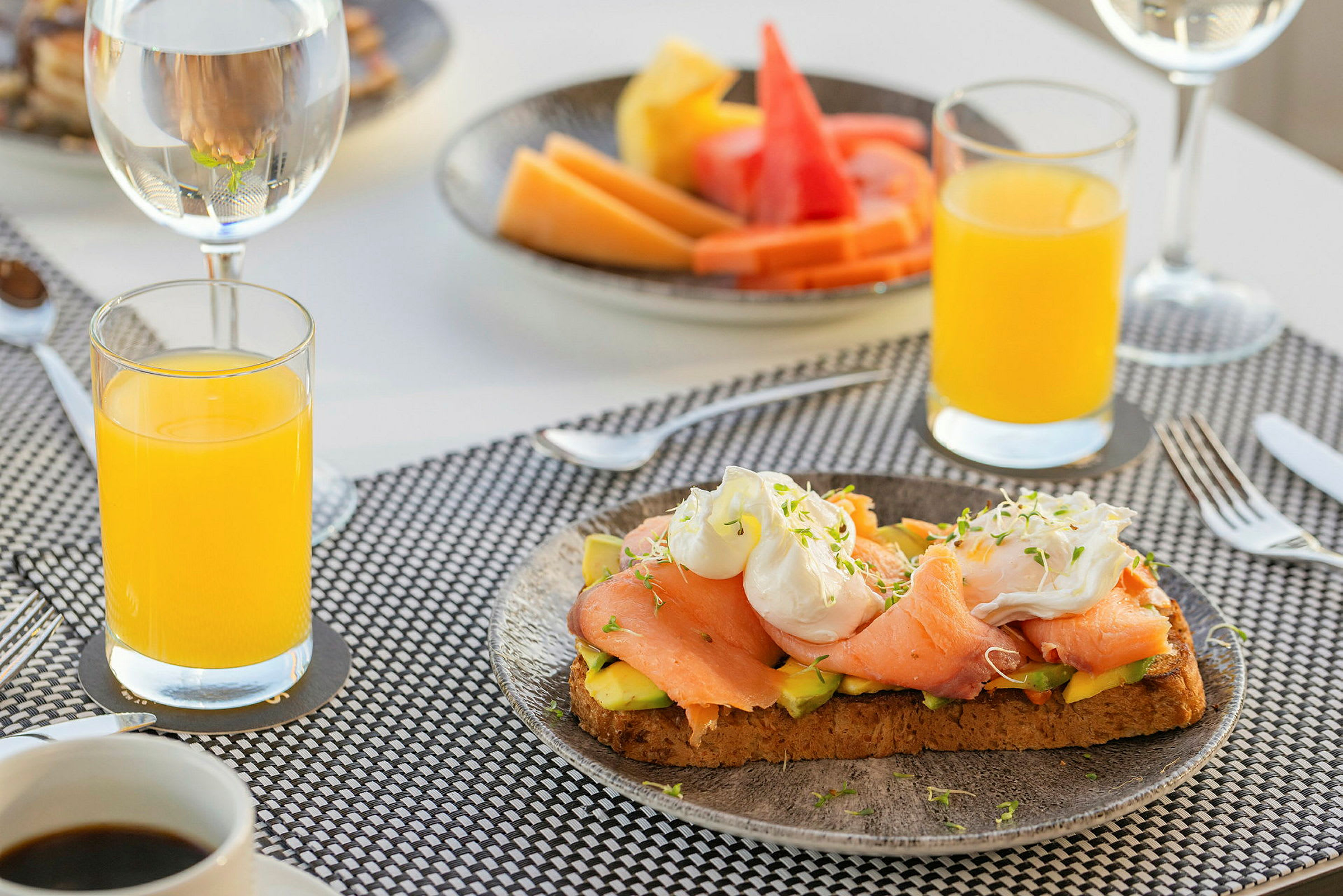 En frukost med juice, kaffe, toast med lax och avokado, och en fat med frukt. (AI-genererad text)