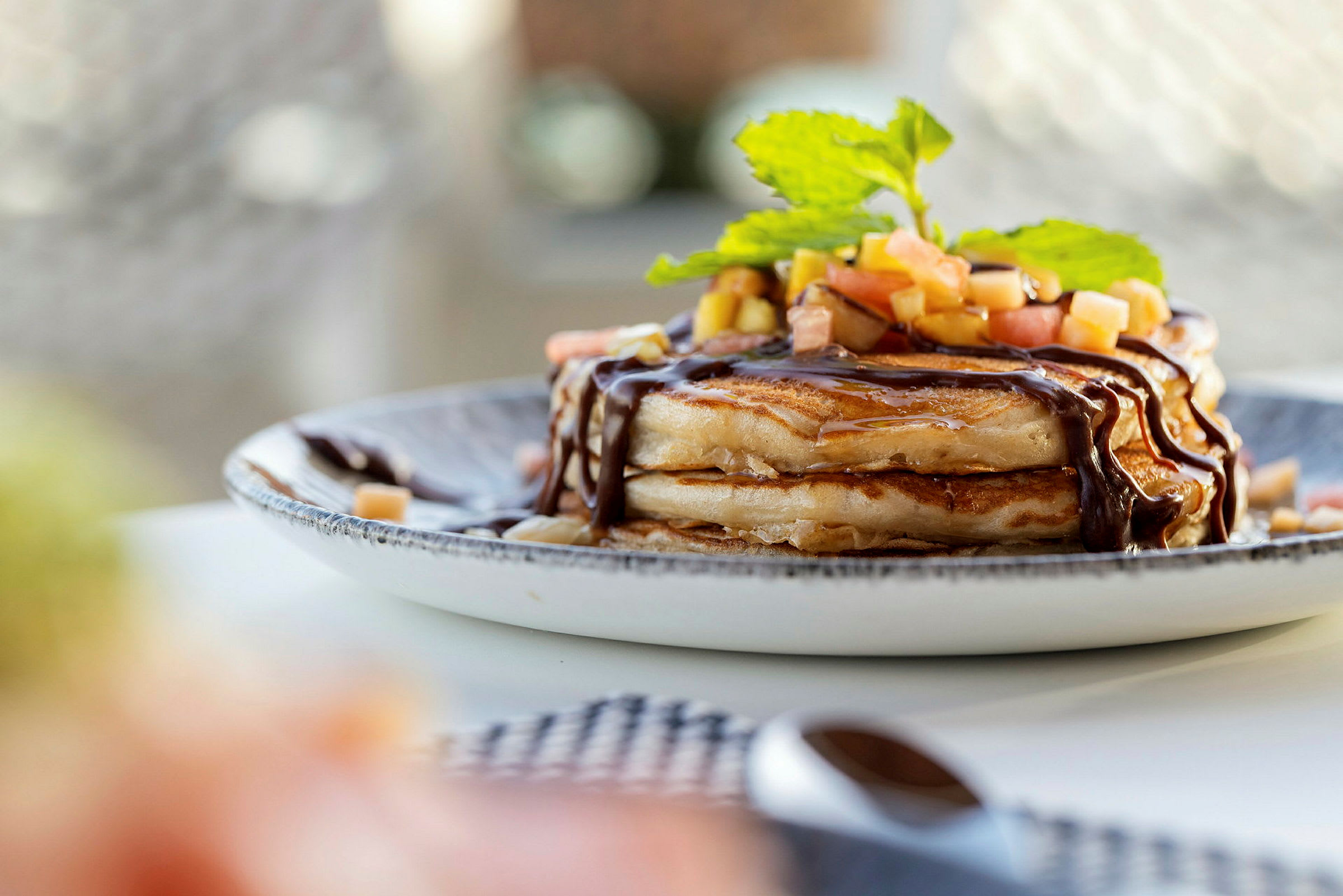 En hög av pannkakor med topping av färsk frukt och chokladsås på en tallrik. (AI-genererad text)