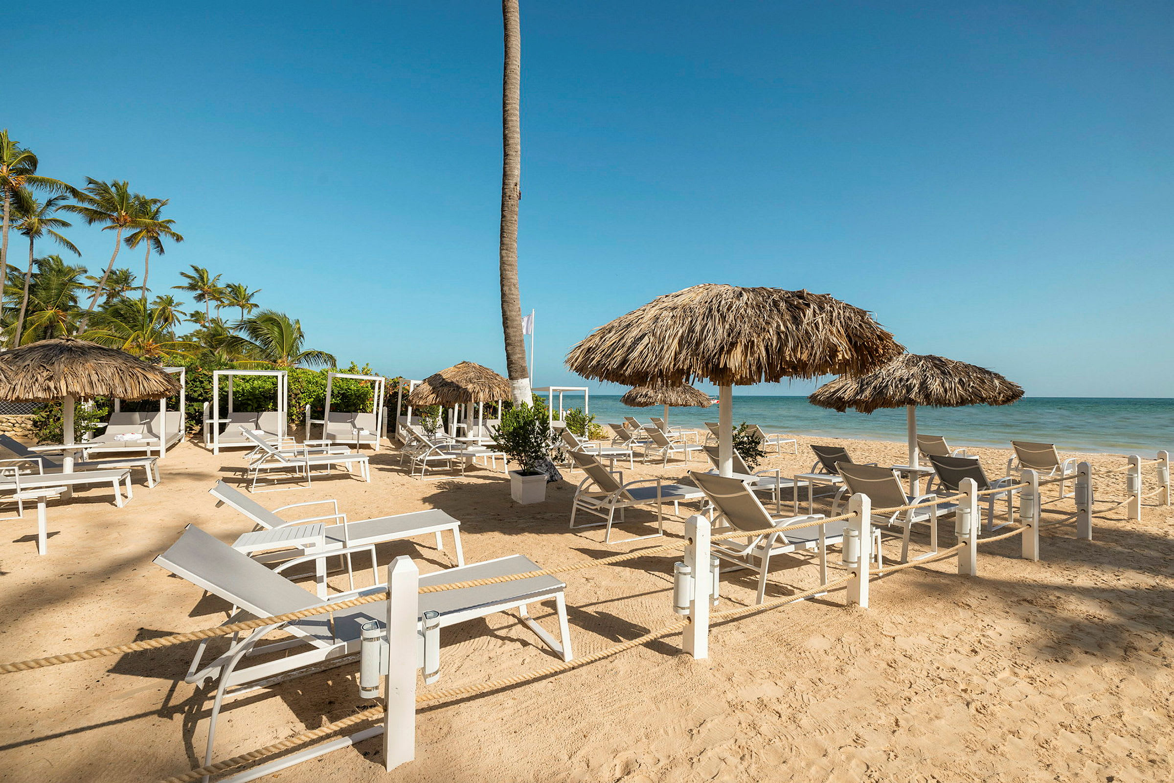 Solstolar och parasoll står uppställda på en sandig strand med lugnt hav i bakgrunden. (AI-genererad text)
