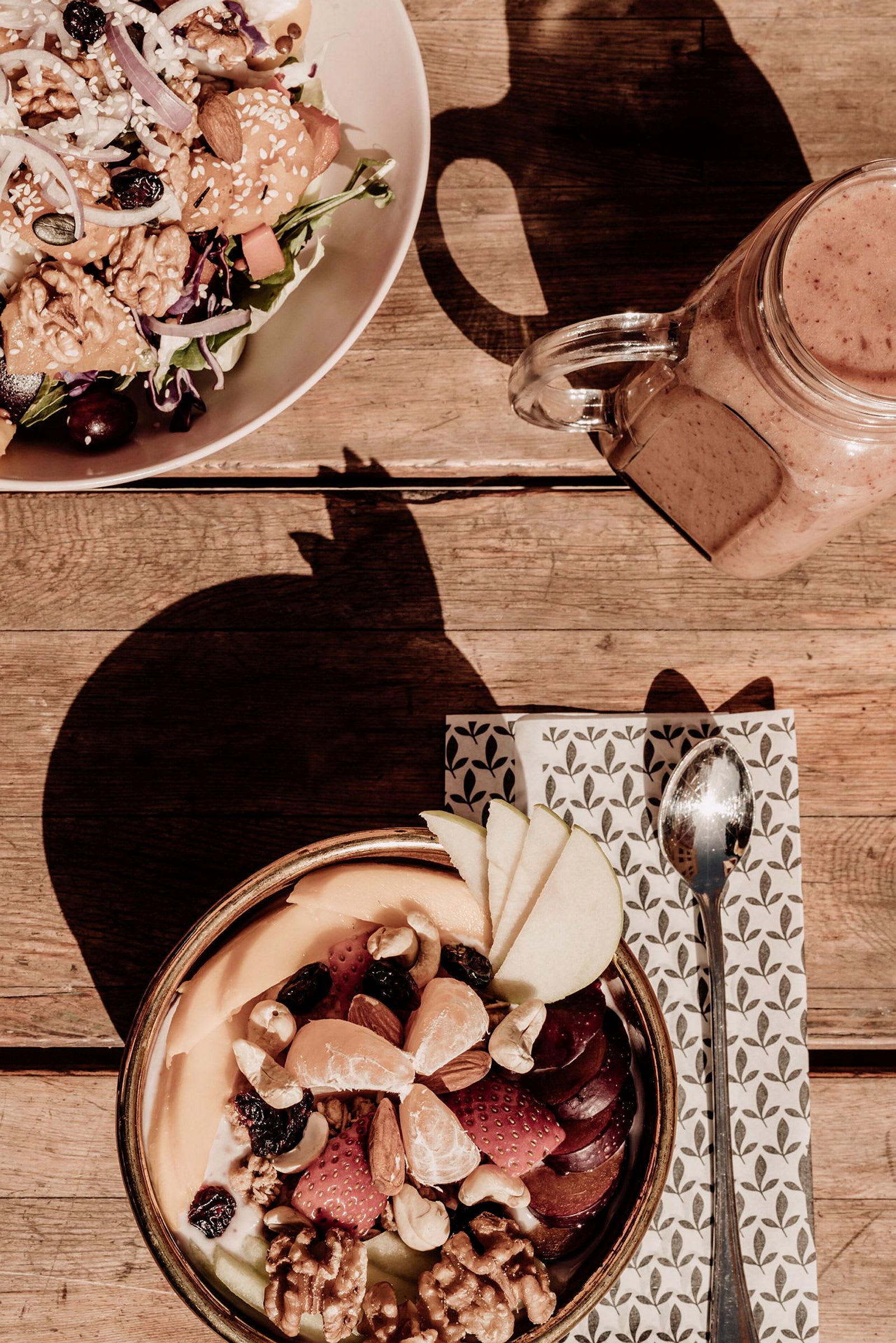 En måltid med blandad sallad och en skål fylld med frukt och nötter på ett träbord. (AI-genererad text)