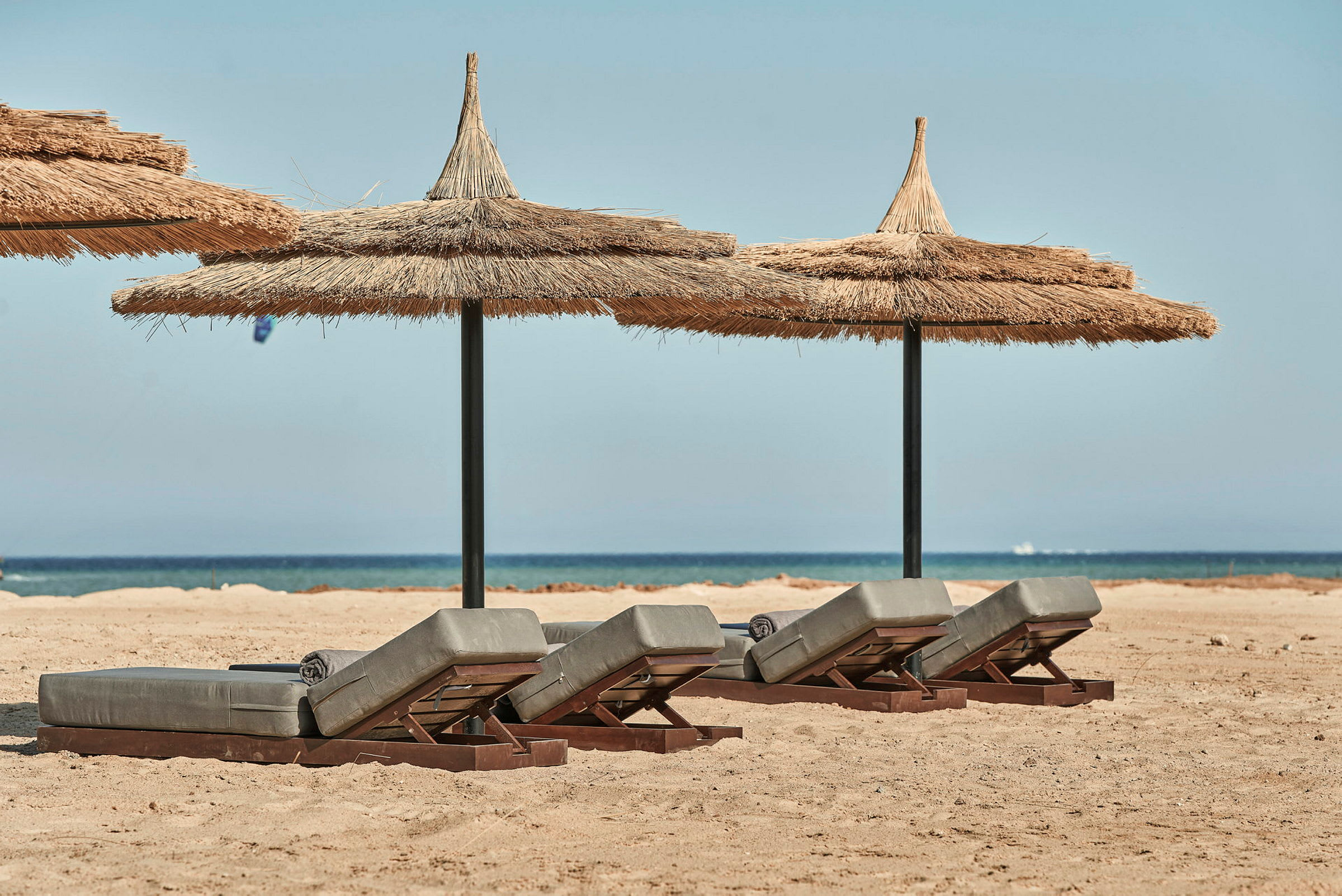 Solstolar med halmtak på sandstrand med hav i bakgrunden. (AI-genererad text)