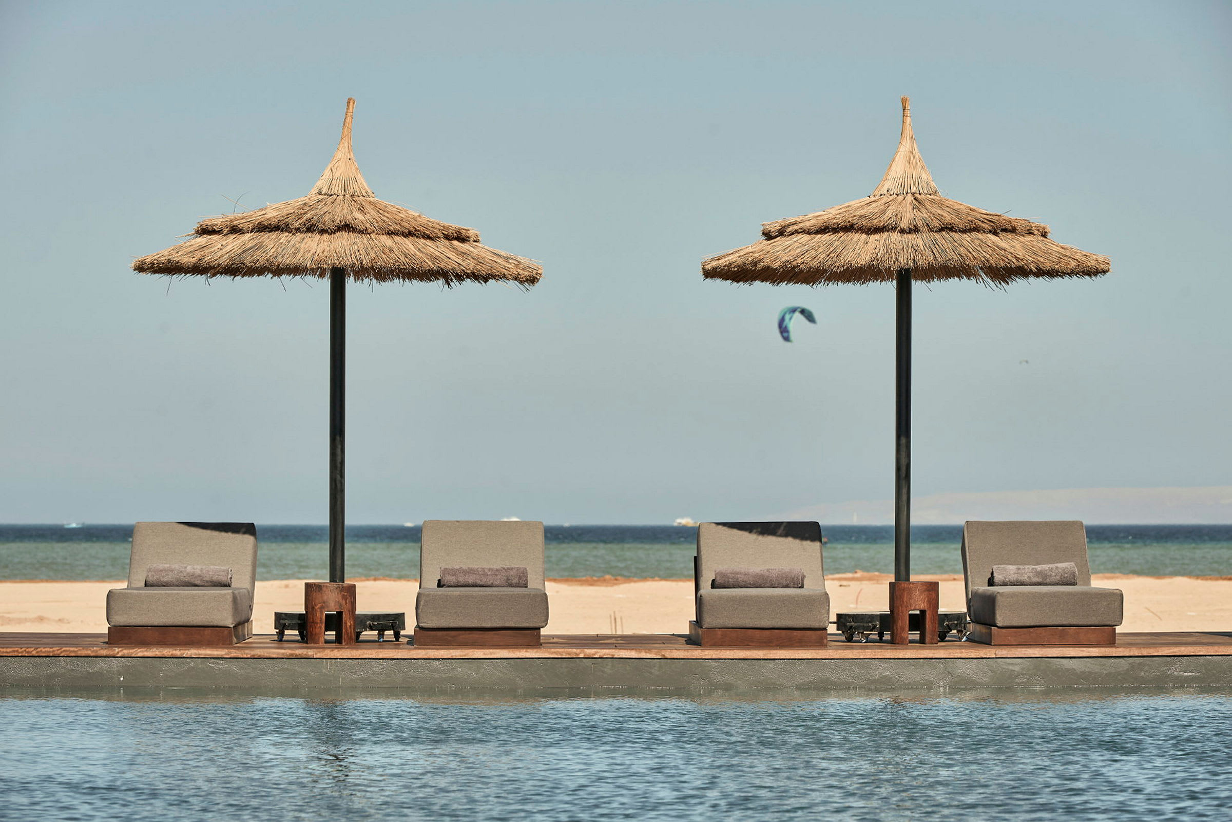 Solstolar och parasoller vid en pool med utsikt över stranden och havet. (AI-genererad text)