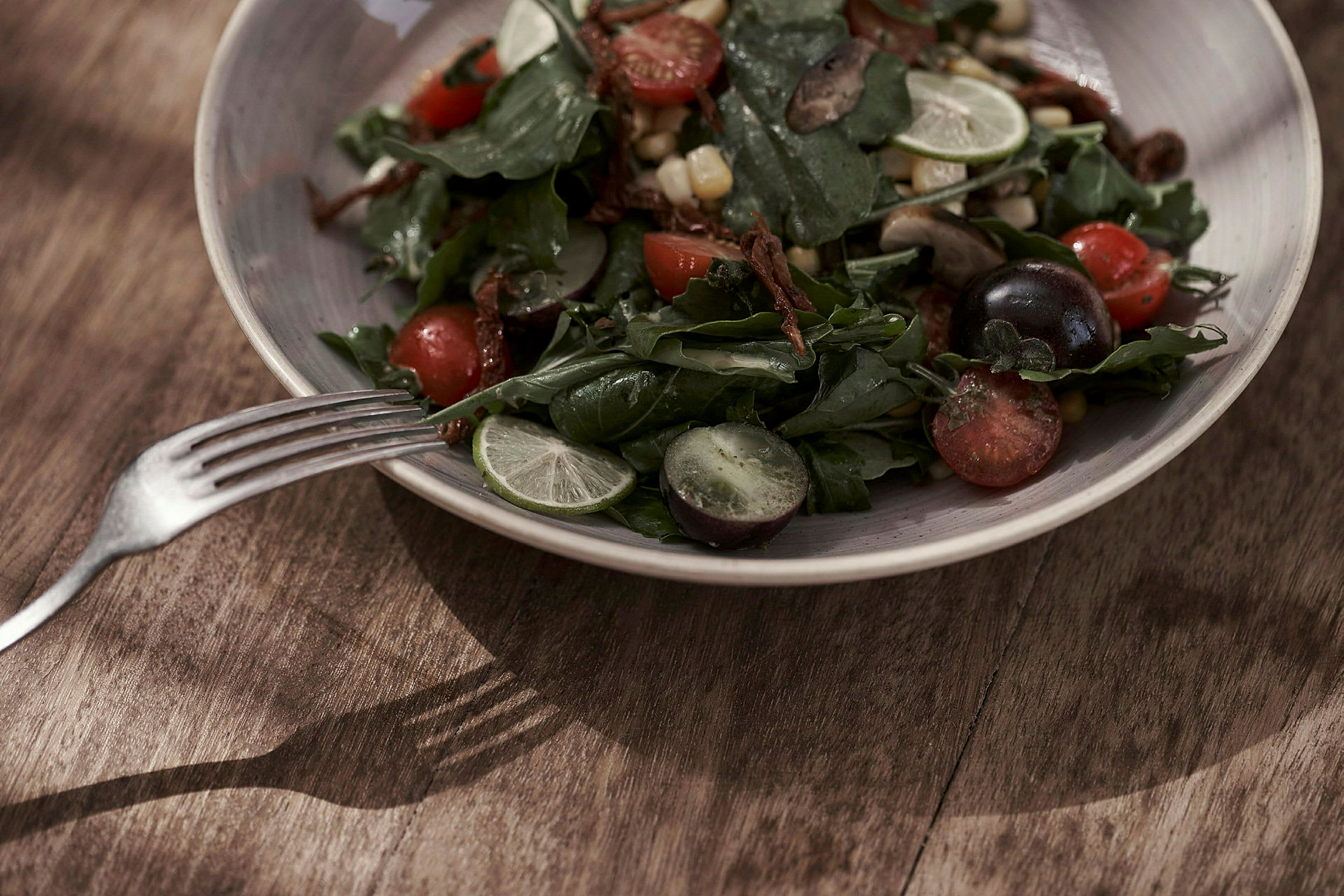 En sallad med olika grönsaker och frukter serverad på en tallrik med en gaffel bredvid. (AI-genererad text)