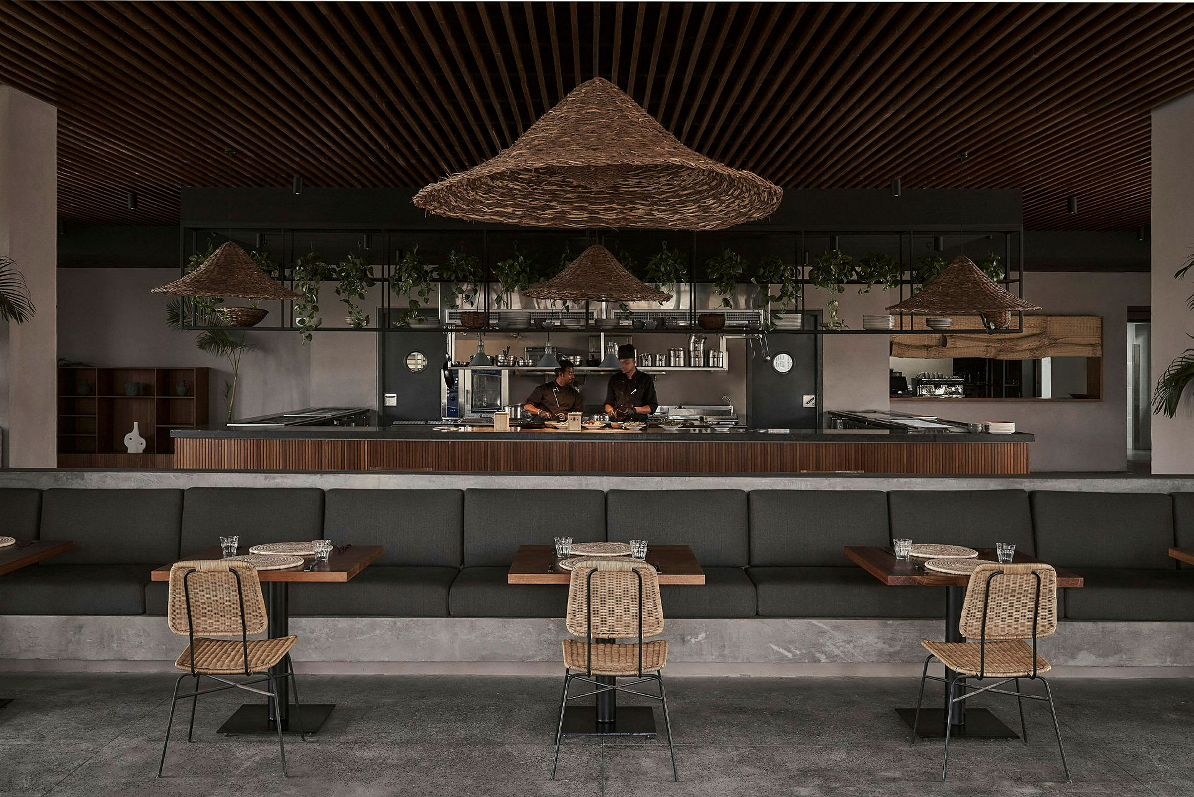 En restaurang med sittplatser och en öppen köksmiljö med dekorativa korglampor och grönska. (AI-genererad text)