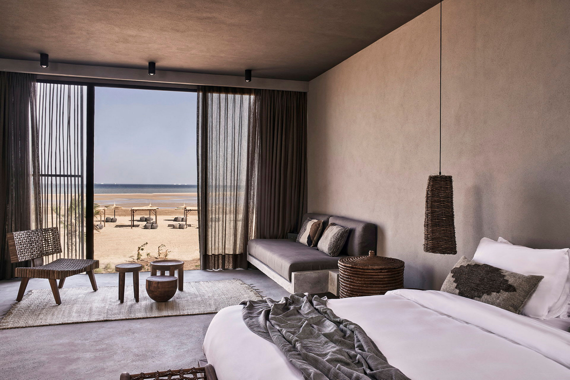 Ett hotellrum med säng, soffa och utsikt mot stranden genom en stor glasdörr. (AI-genererad text)