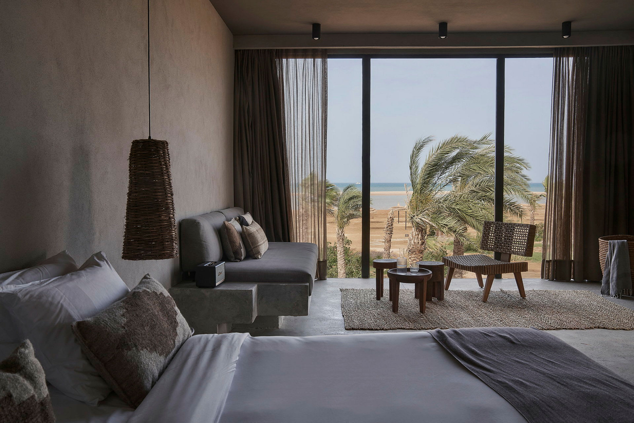 Modernt hotellrum med säng, sittgrupp och stora fönster mot strand och palmer. (AI-genererad text)