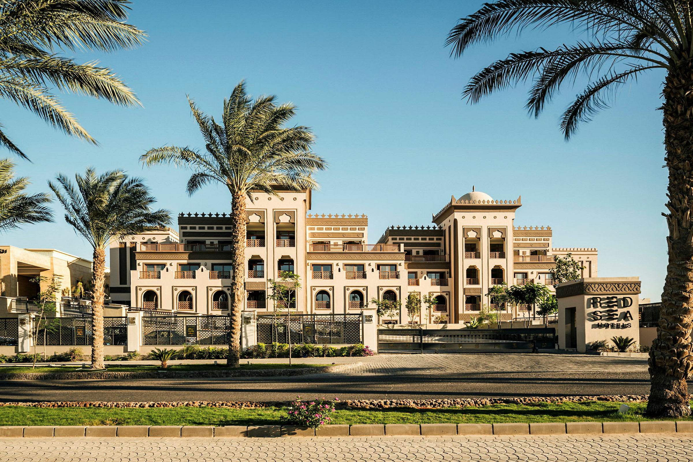 Ett elegant hotellkomplex i arabisk stil med palmer i förgrunden under en klarblå himmel. (AI-genererad text)