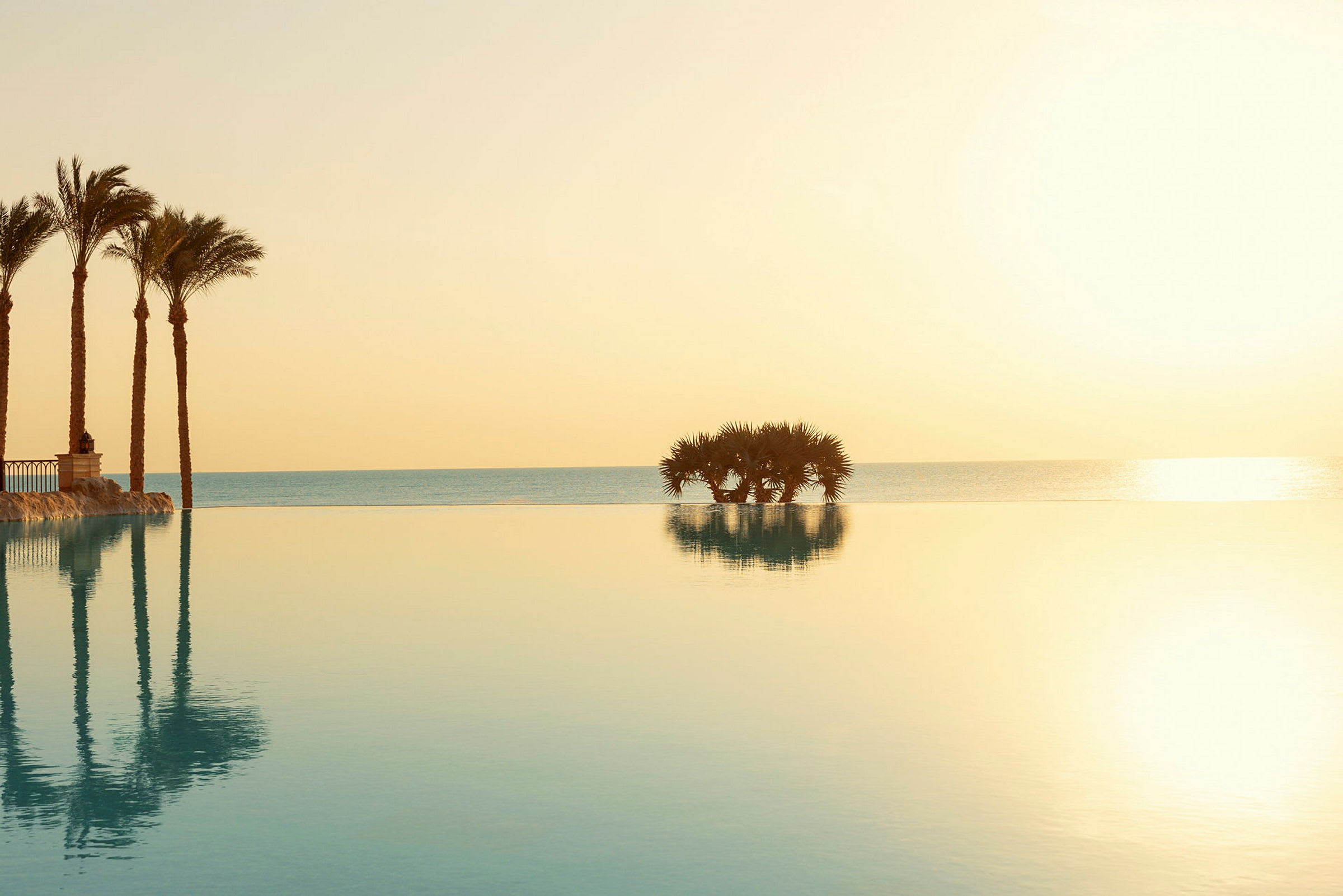 Infinitypool med utsikt över havet och solnedgång, palmer i förgrunden. (AI-genererad text)