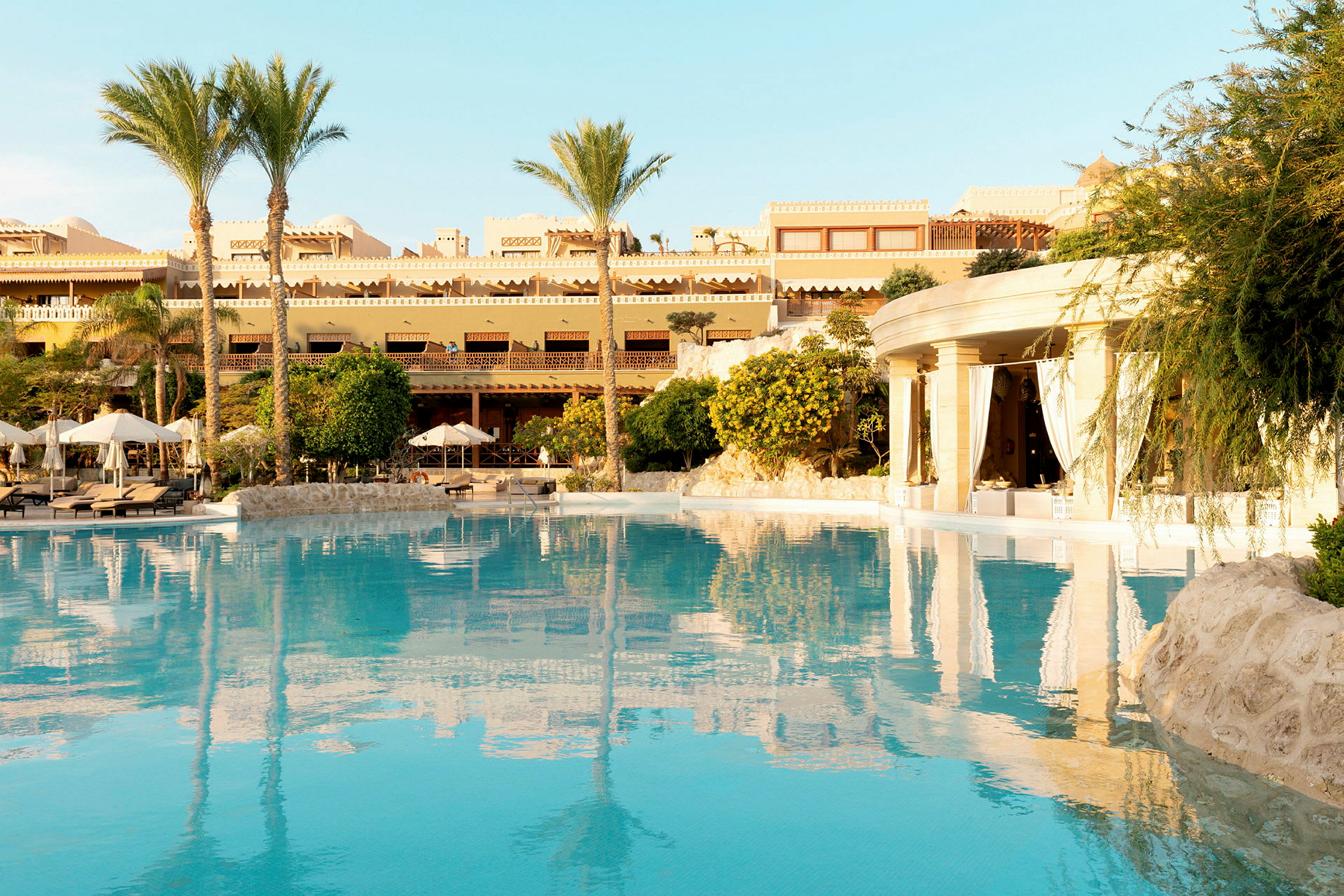 Hotellområde med pool, parasoller och byggnader i bakgrunden. (AI-genererad text)