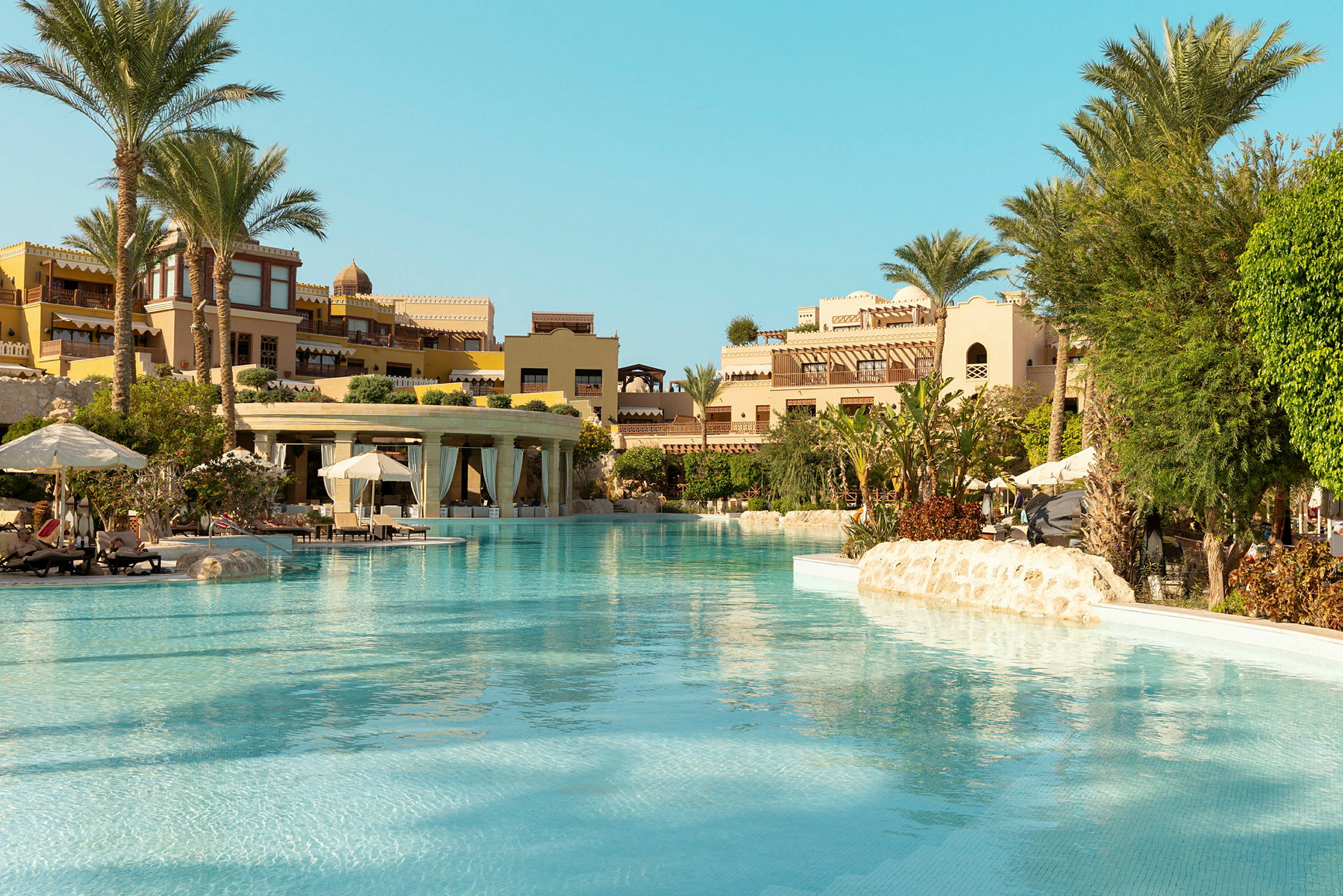 Bild av en hotellpool omgiven av solstolar, parasoller och grönskande växter. (AI-genererad text)