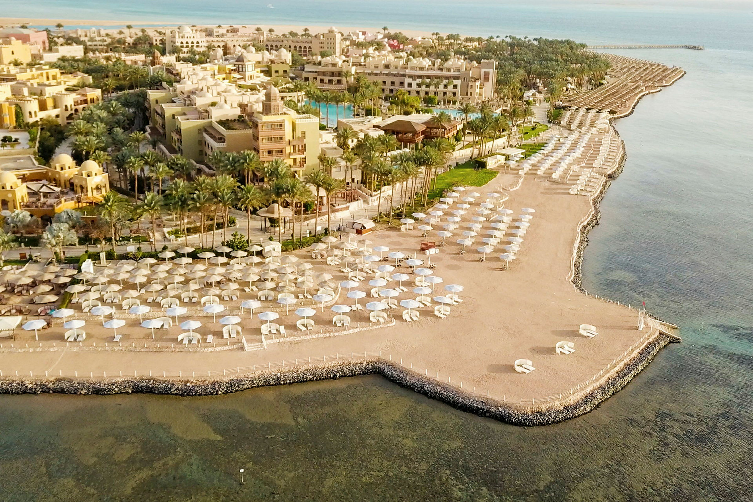 Flygfoto av en strand med parasoller och hotellbyggnader i bakgrunden. (AI-genererad text)