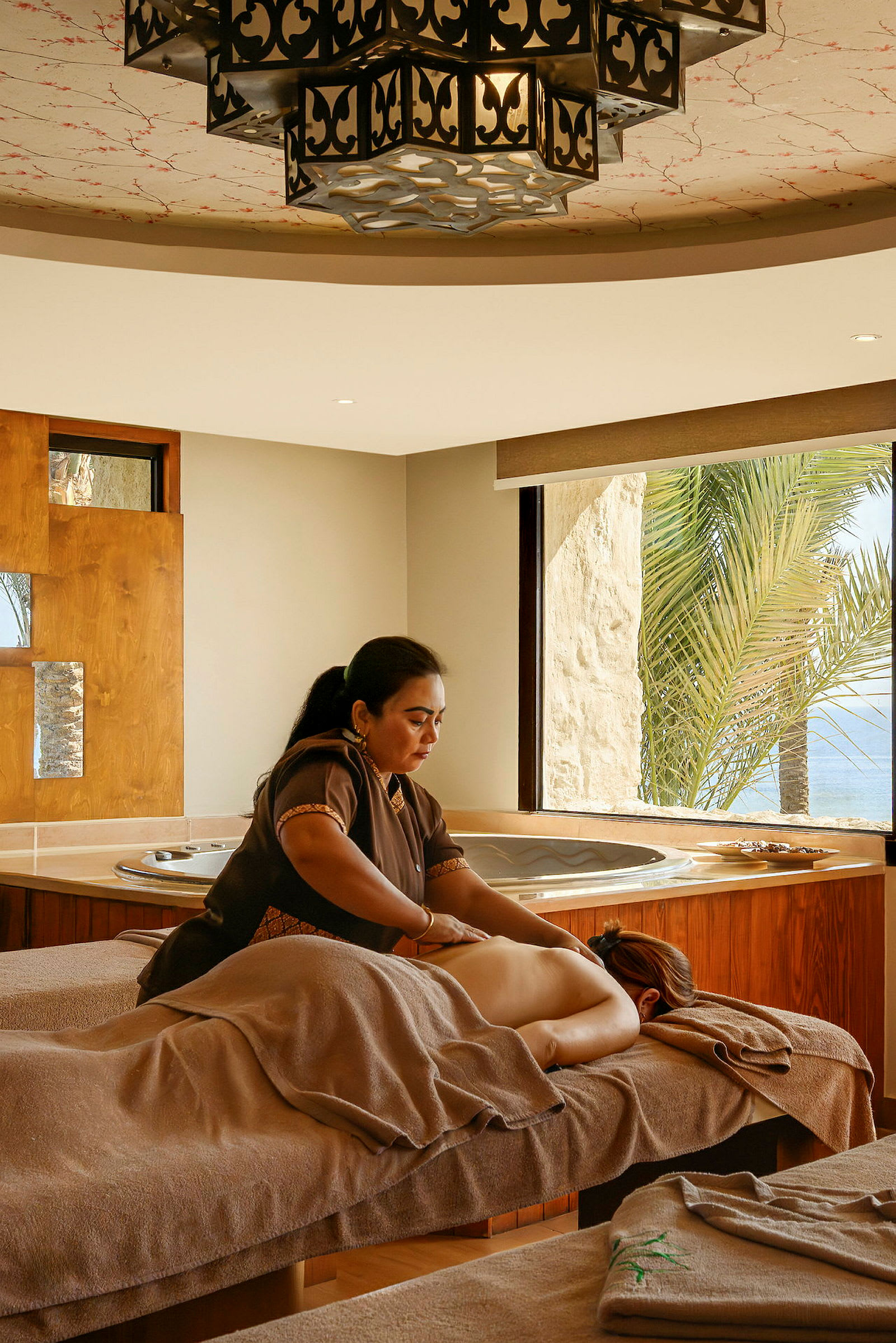 Ett spa med massagebänk och jacuzzi, palmer syns utanför fönstret. (AI-genererad text)