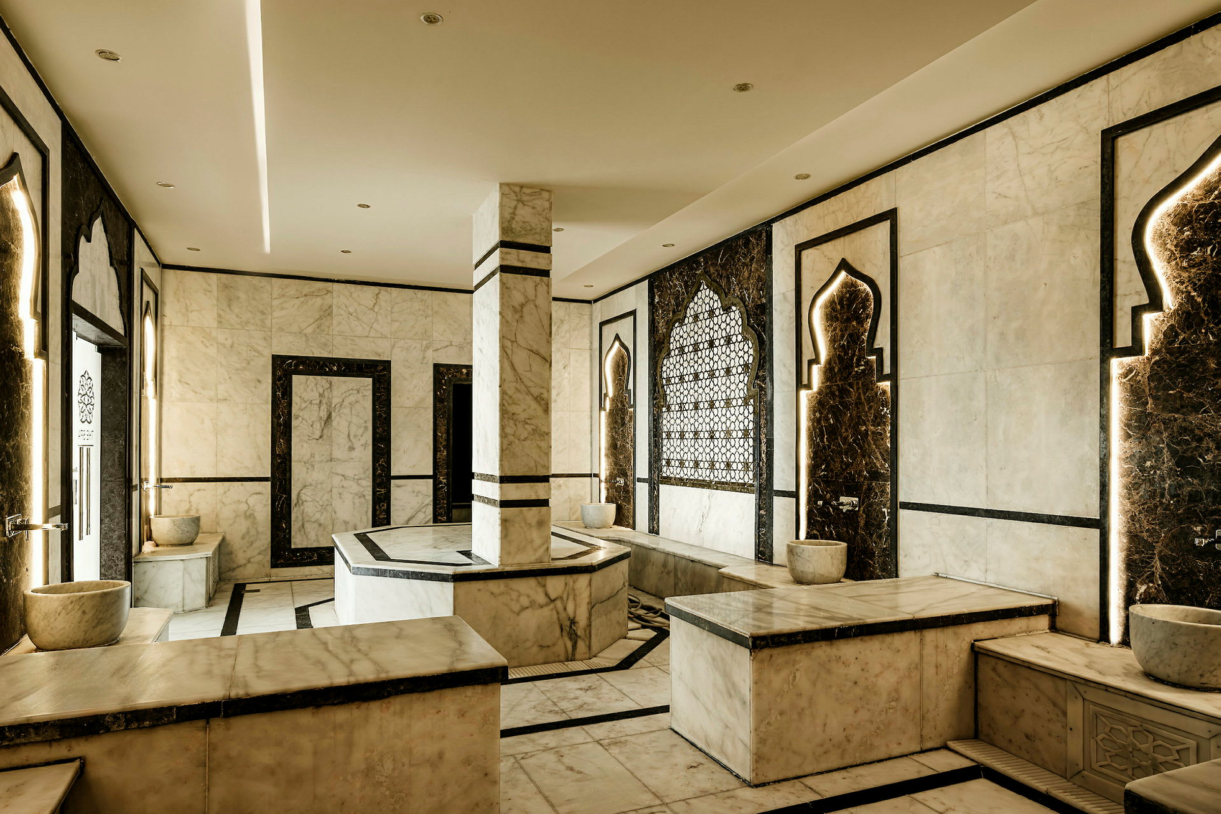 Ett rum i traditionell hamam-stil, med marmorinredning, dekorativa motiv och bänkar. (AI-genererad text)