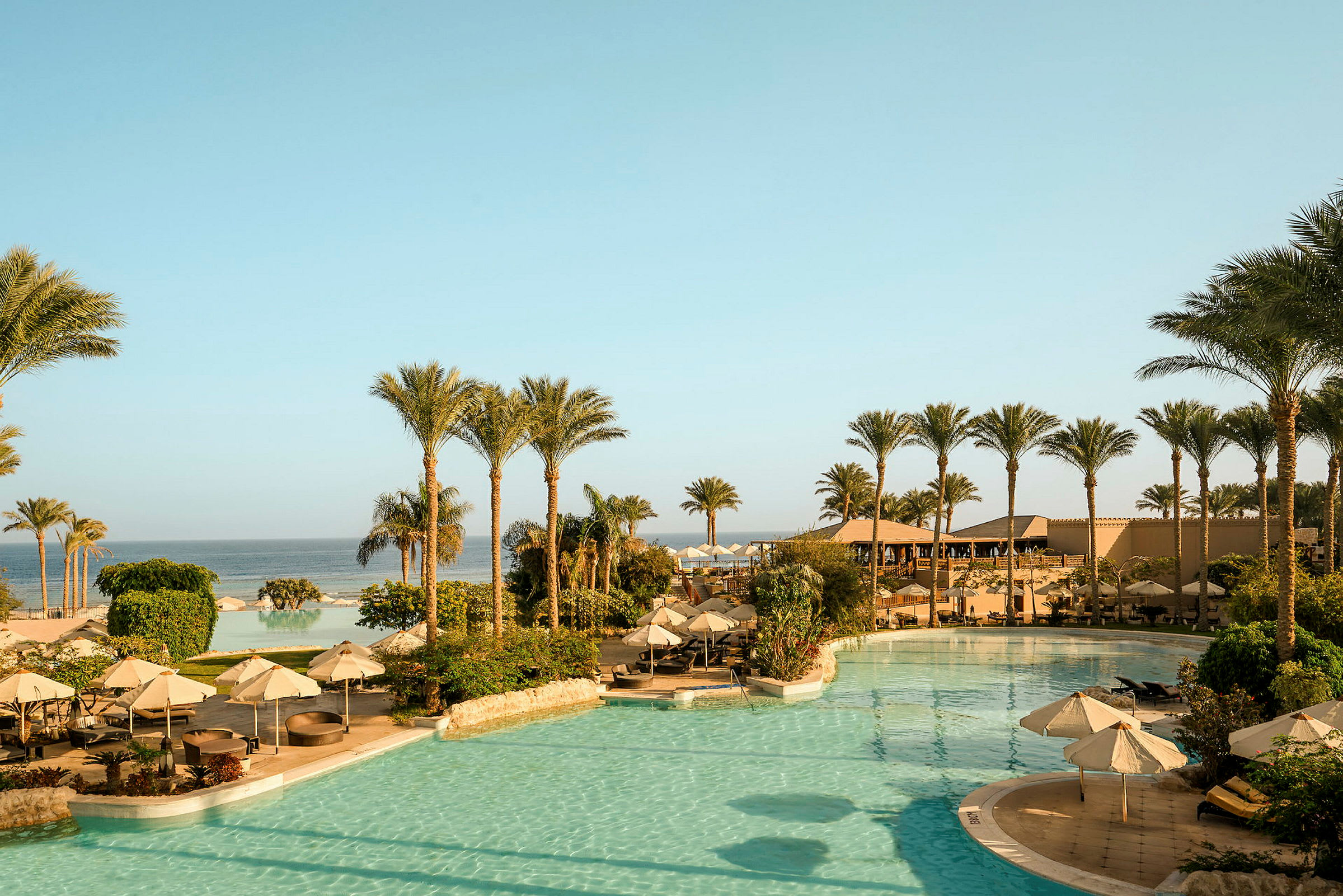 Bild av ett semesterhotell med pool, parasoller och palmer nära havet. (AI-genererad text)