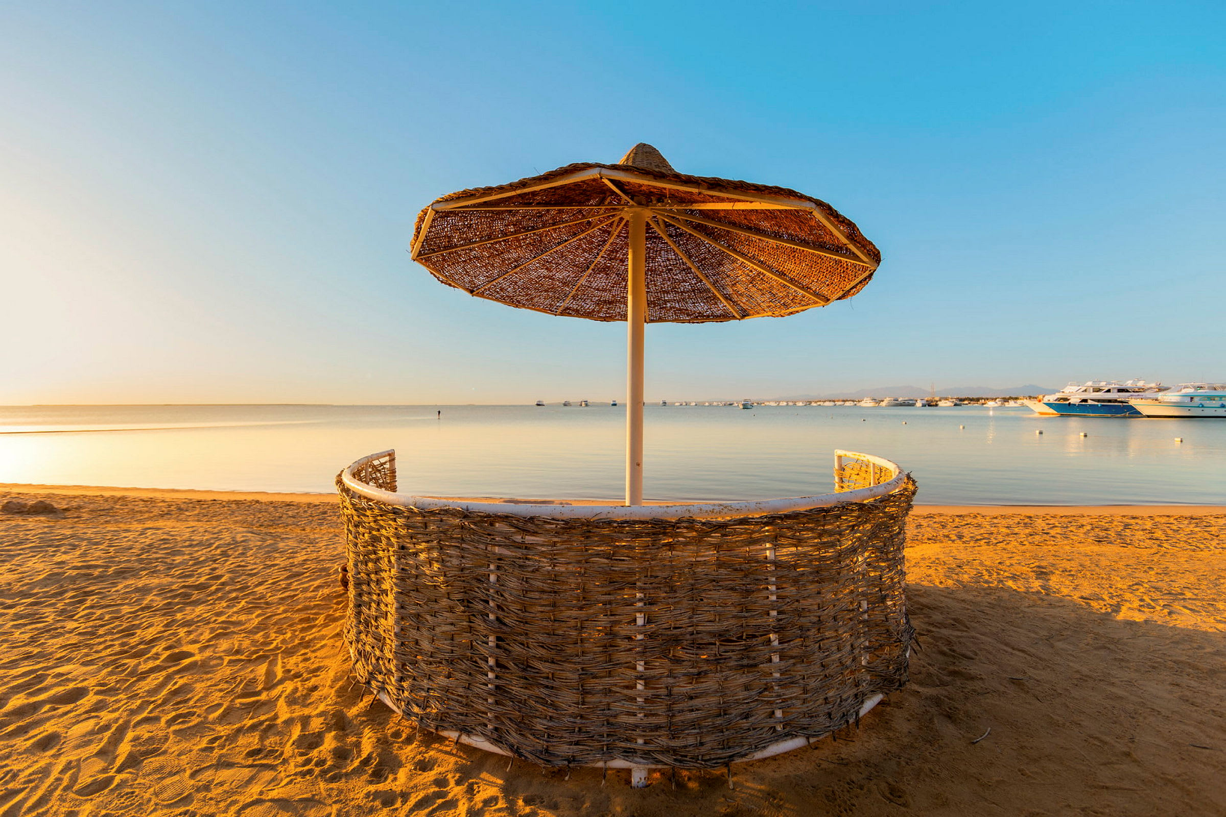 Strand med solskydd av flätad material och hav i bakgrunden. (AI-genererad text)