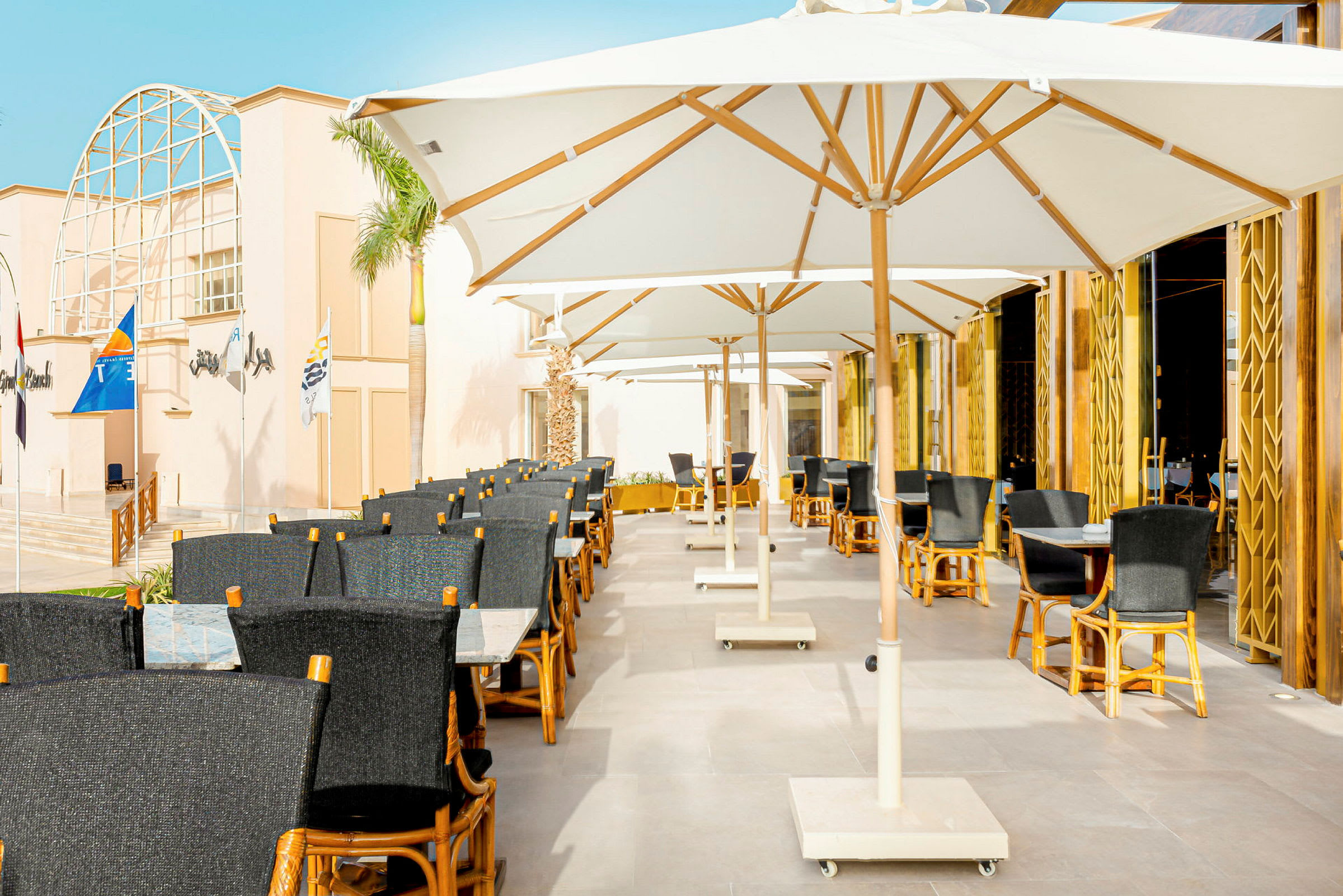 Utomhusrestaurang med vita parasoller och stolar i trä och mörkt tyg. (AI-genererad text)