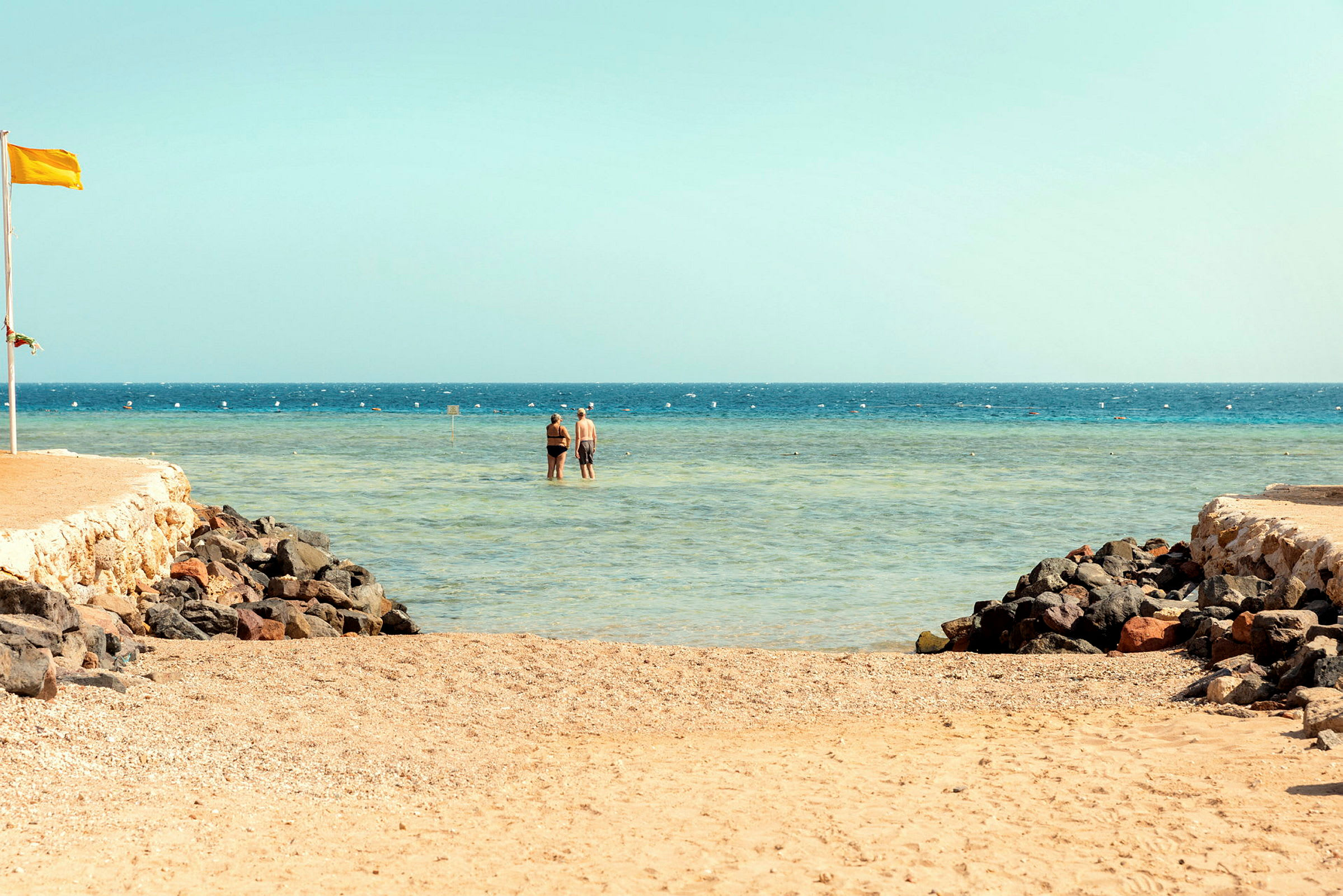 Två personer står i grunt vatten vid en strand. (AI-genererad text)