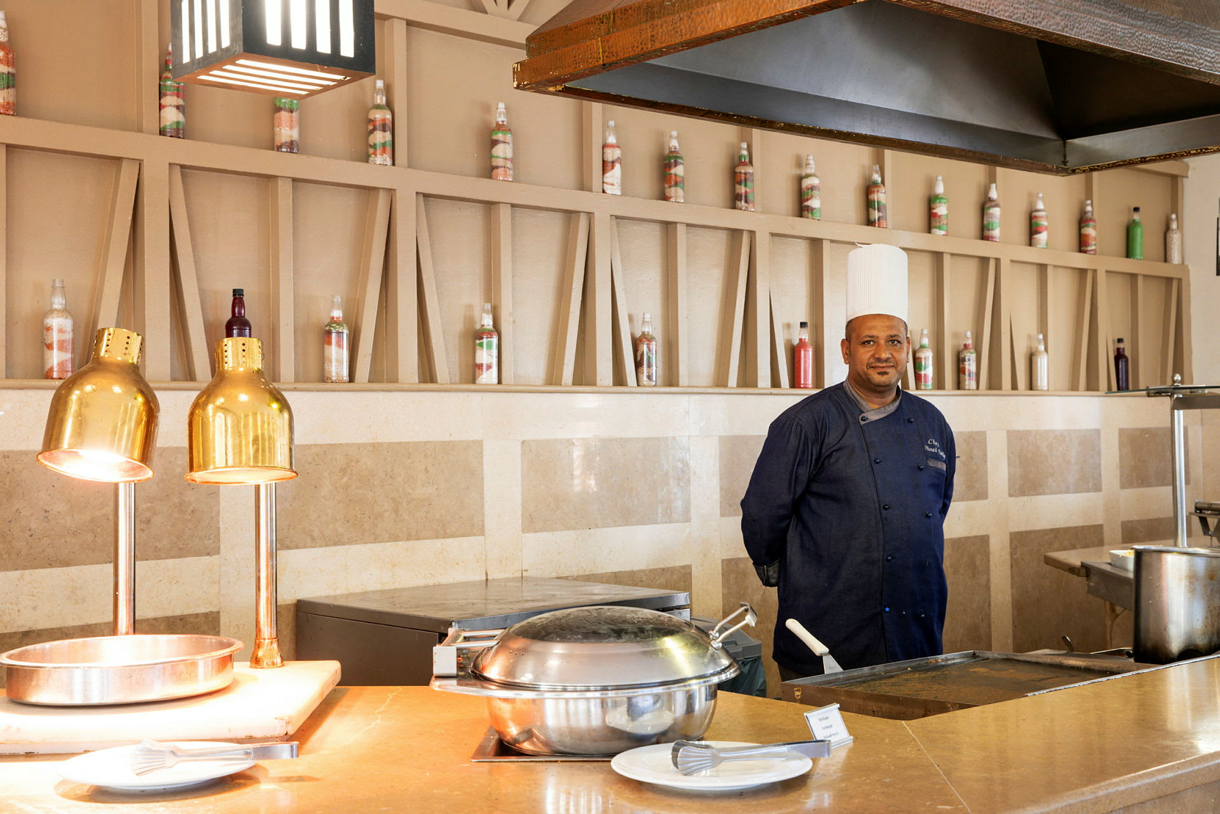 En köksstation med kastruller, tallrikar och värmelampor vid ett hotell. (AI-genererad text)