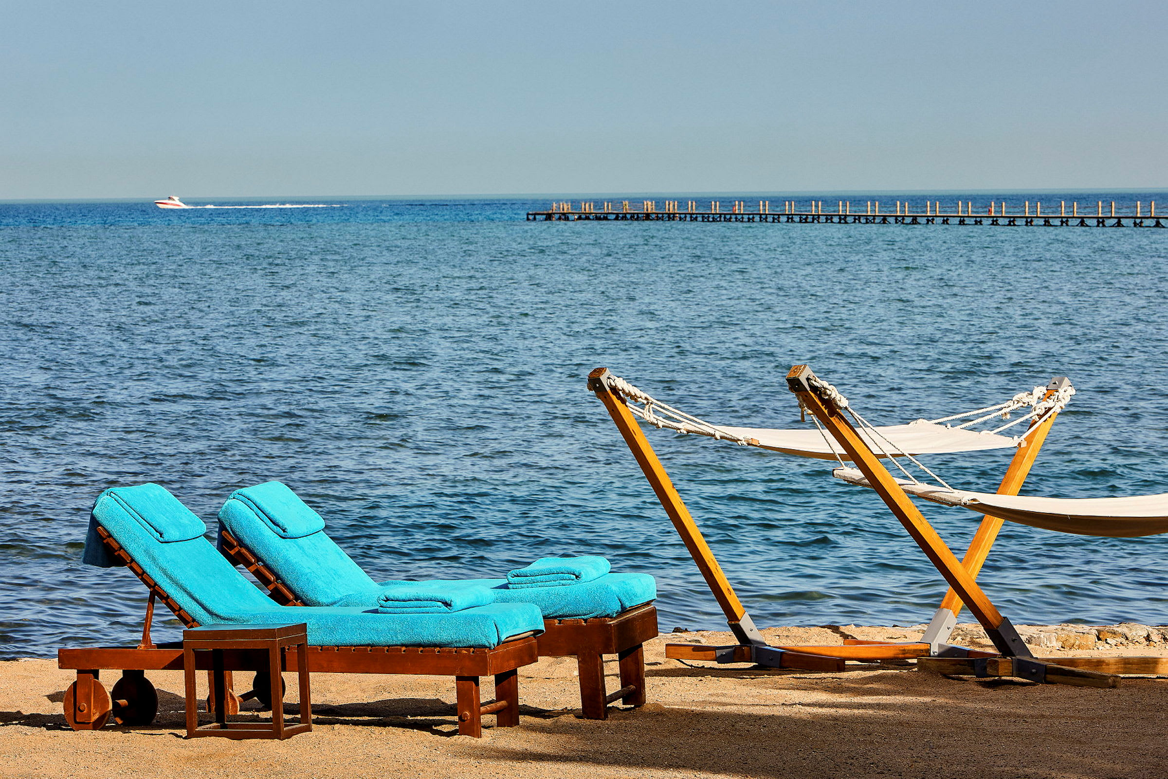 Två solstolar med blå dynor och två hängmattor vid en strand med havsutsikt. (AI-genererad text)