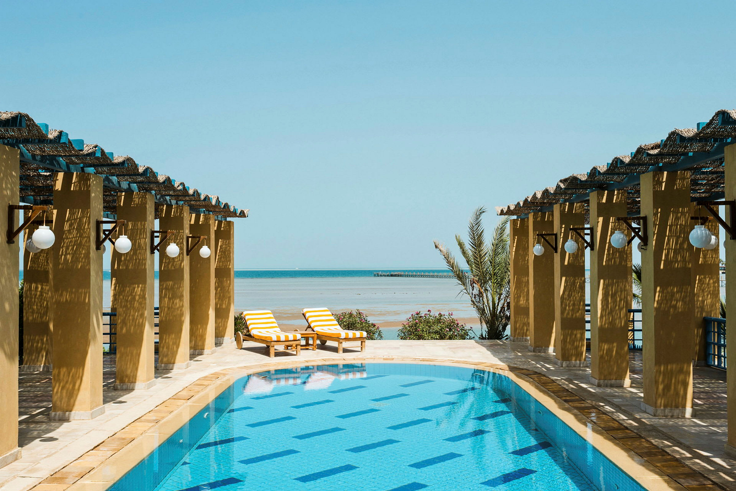 En pool framför en pergola med havet i bakgrunden. (AI-genererad text)