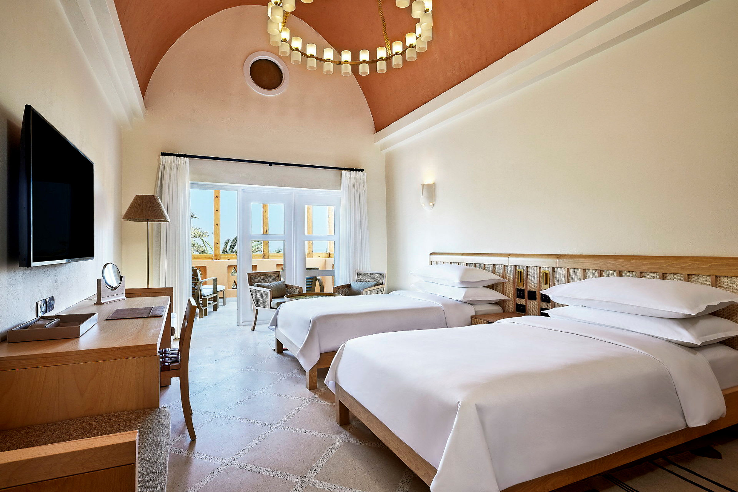 Hotellrum med två enkelsängar, skrivbord och sittgrupp vid balkongen. (AI-genererad text)