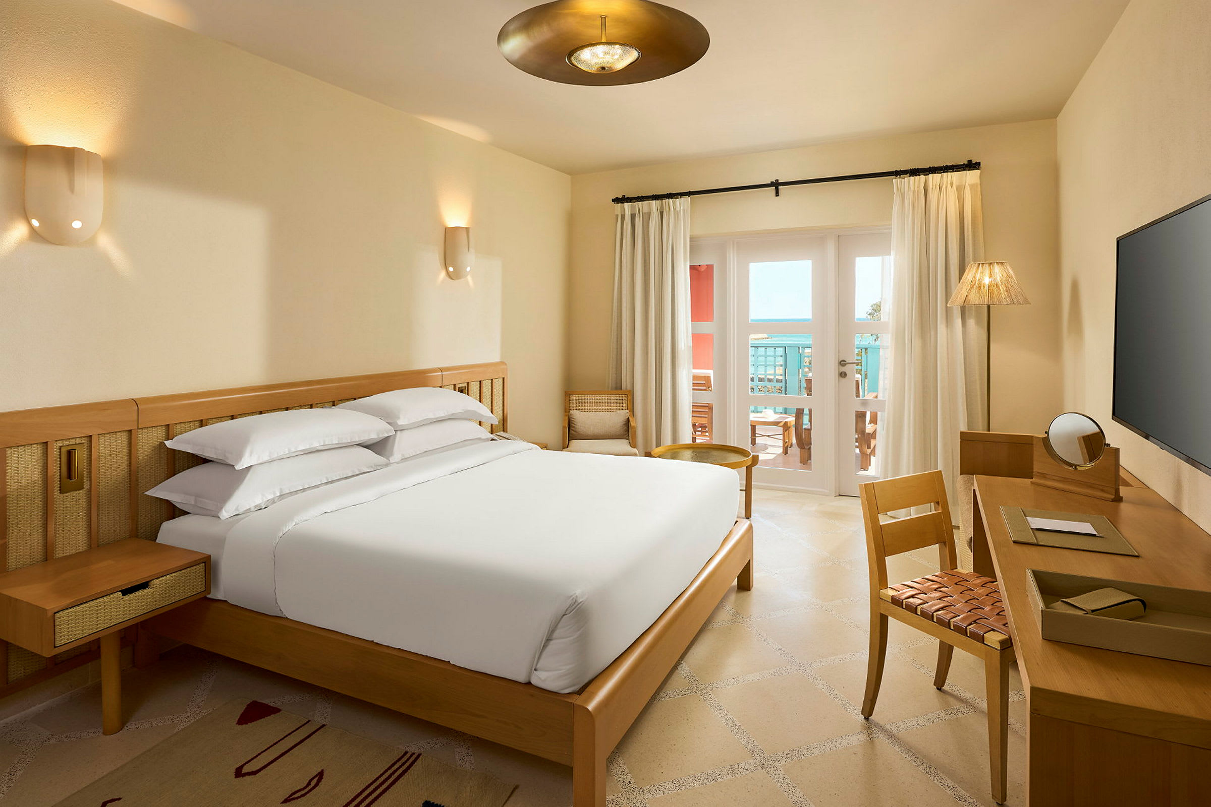 Ett hotellrum med en säng, skrivbord och en balkong med utsikt. (AI-genererad text)