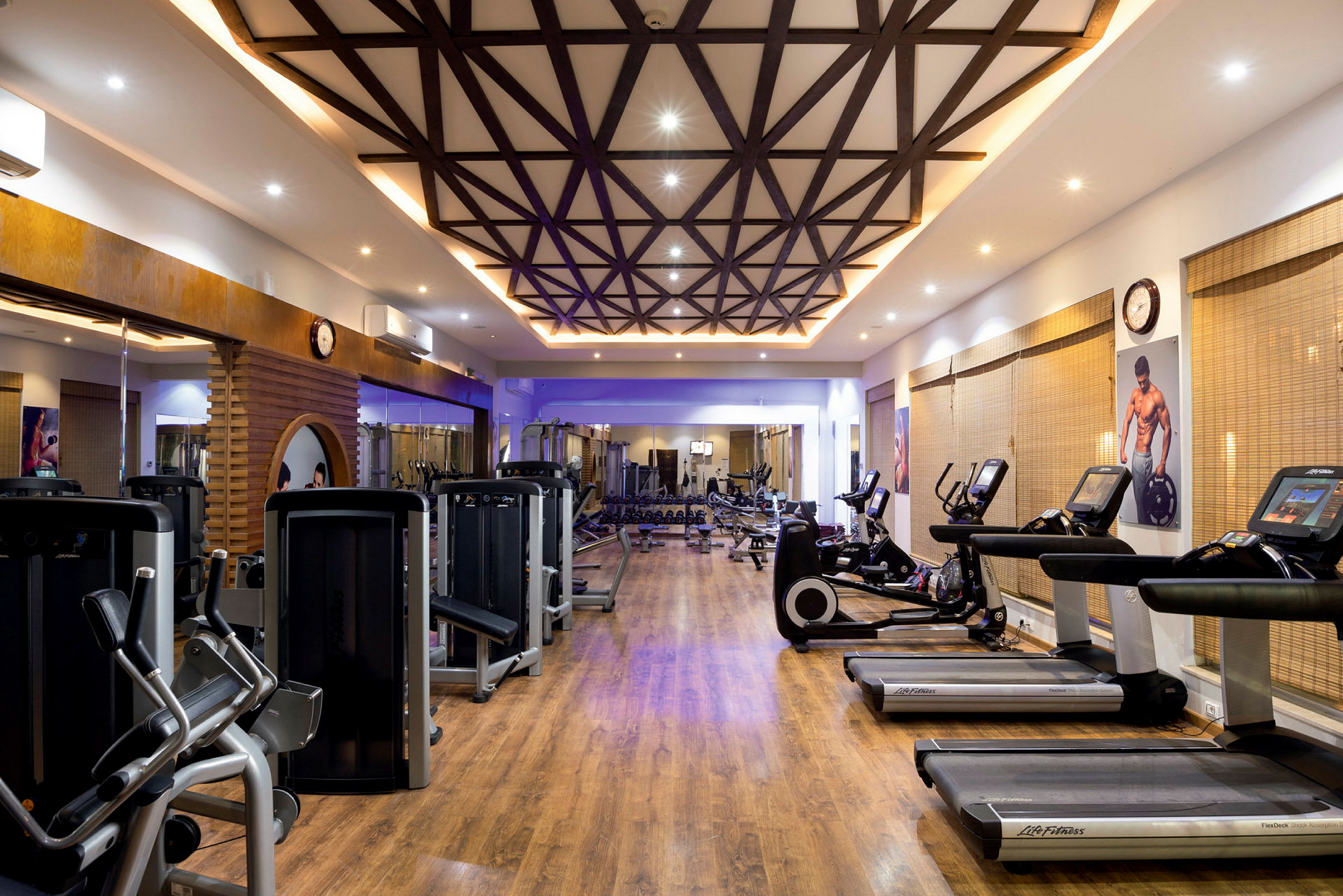 Ett välutrustat gym med flera träningsmaskiner och trädekorationer i taket. (AI-genererad text)