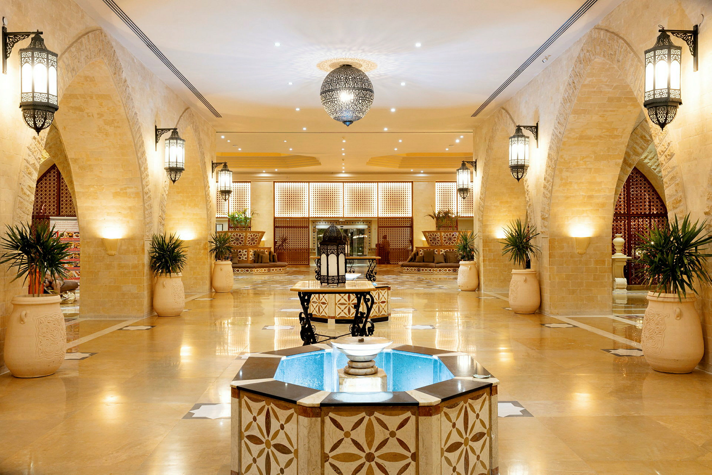 Hotellobby med ljus inredning, ornamenterade valvbågar och central fontän. (AI-genererad text)