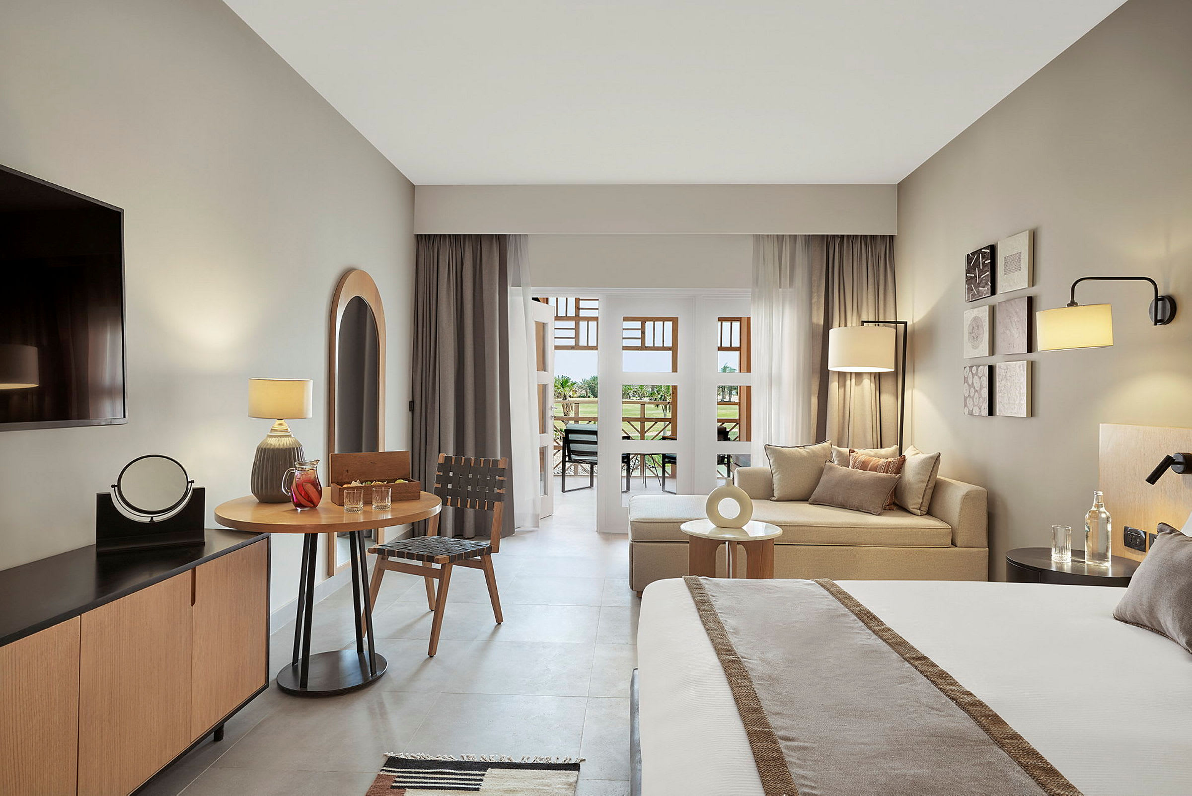 Ett modernt hotellrum med gråa och beige färgtoner, inklusive en säng, sittgrupp, bord och en balkong. (AI-genererad text)