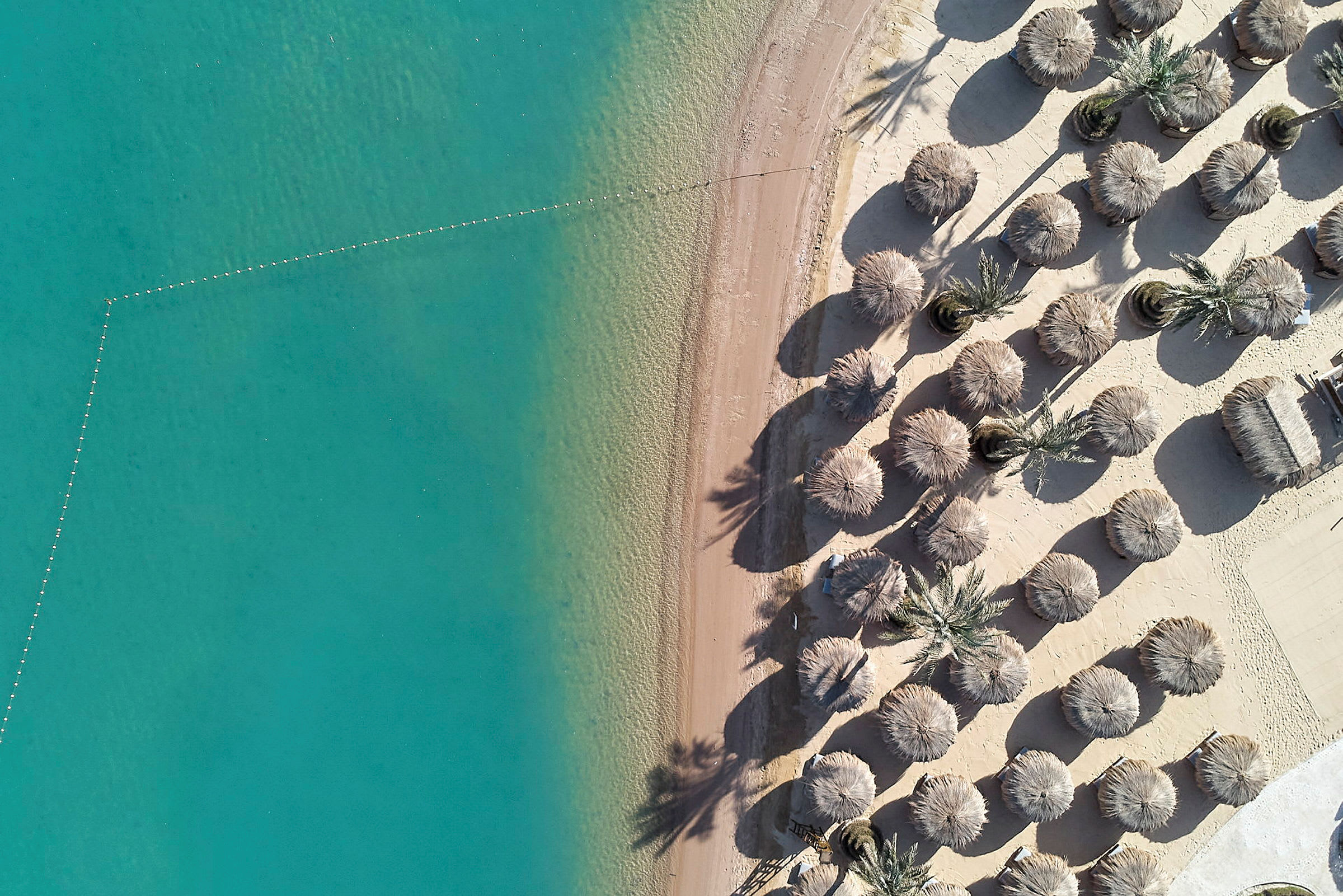 Flygbild av en sandstrand med turkost vatten och parasoller. (AI-genererad text)
