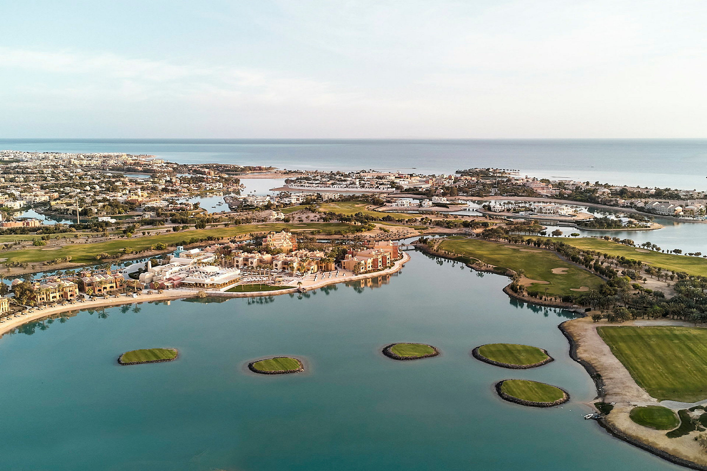 Flygfoto över en resort med byggnader, grönområden och vattenstråk. (AI-genererad text)