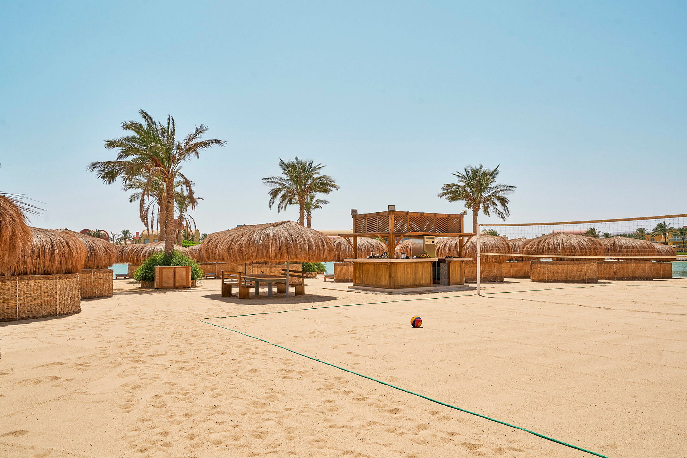 Strand med sand, palmer och parasoll samt en beachvolleybollplan. (AI-genererad text)