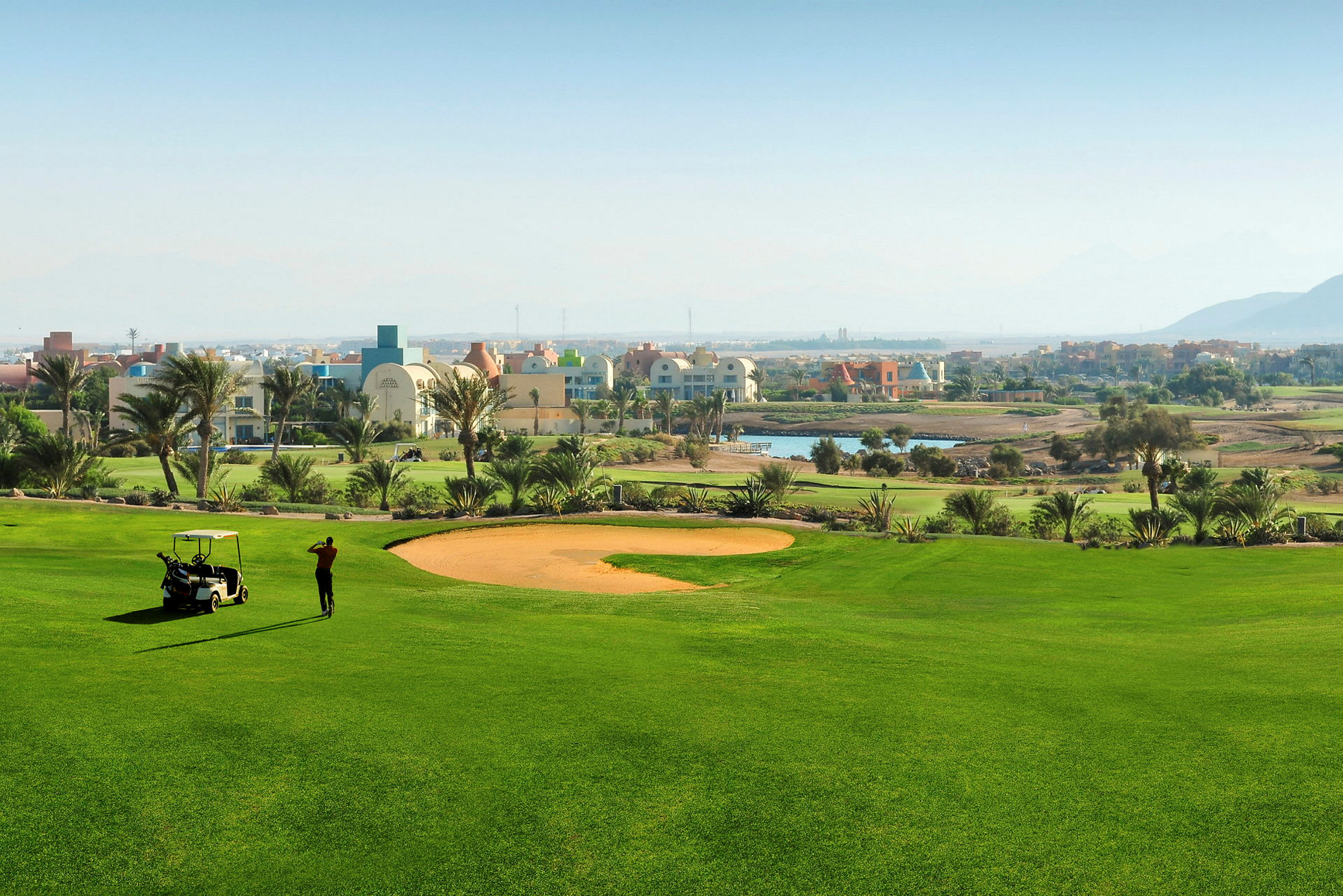 Grön golfbana med en golfspelare och en golfbil i förgrunden. (AI-genererad text)