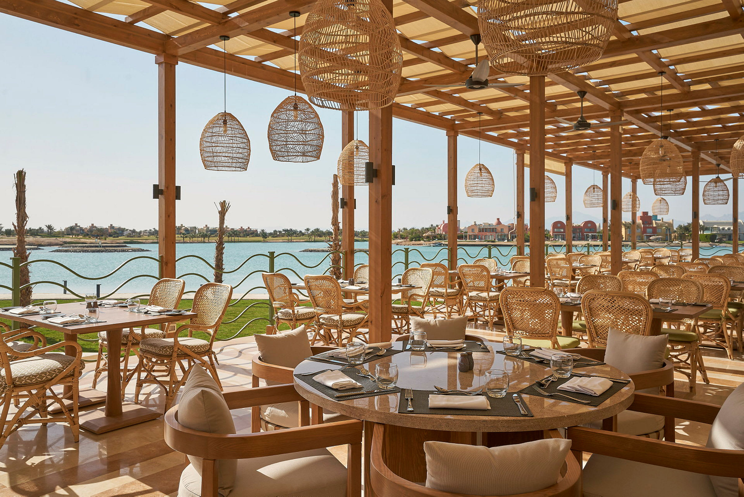 Restaurang med flätade stolar och bord med utsikt över vattnet. (AI-genererad text)