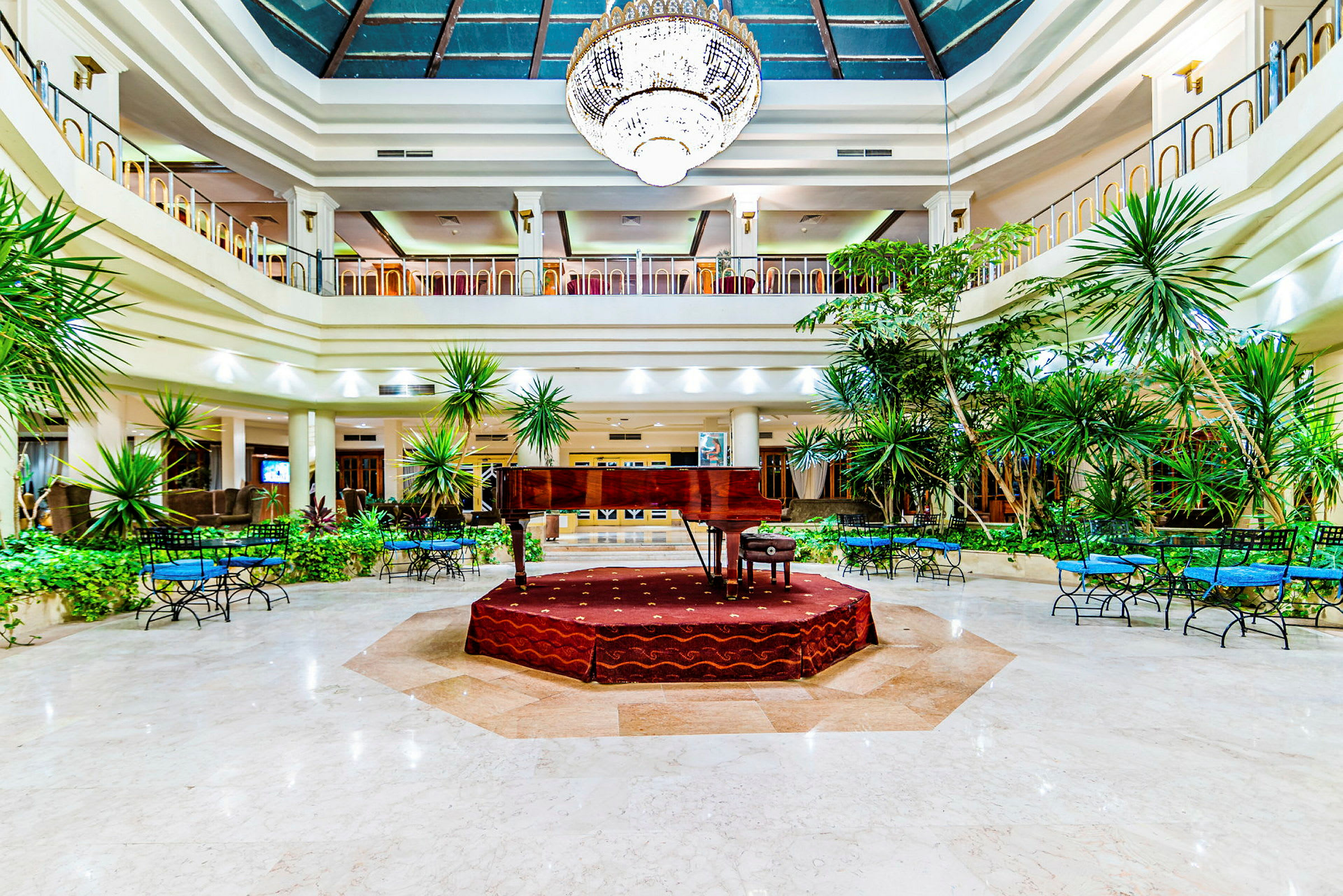 En flygel placerad på en upphöjd scen i en rymlig hotellobby med växtdekorationer. (AI-genererad text)
