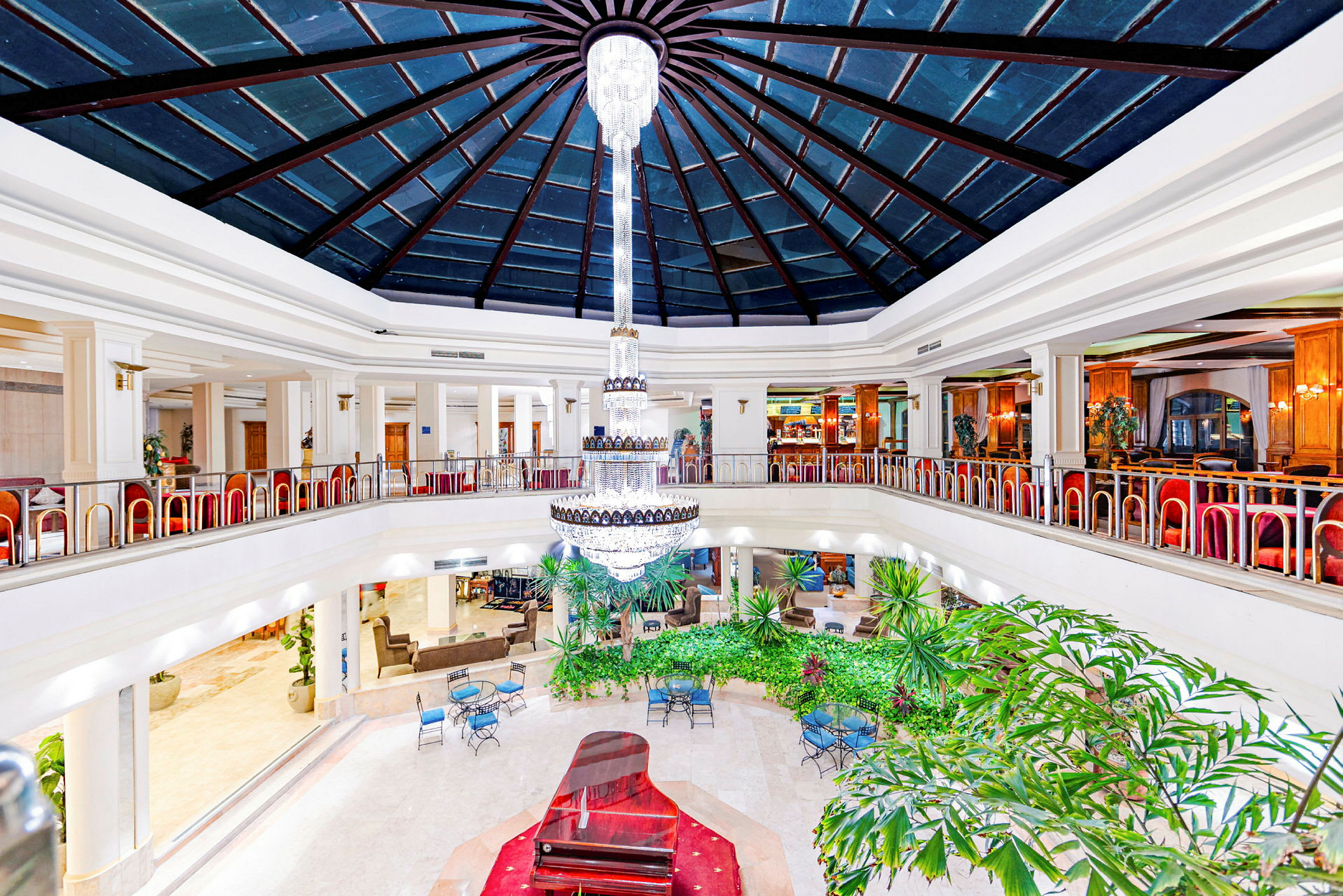 Interiör med ett atrium, en stor kristallkrona, grönska och sittmöbler. (AI-genererad text)