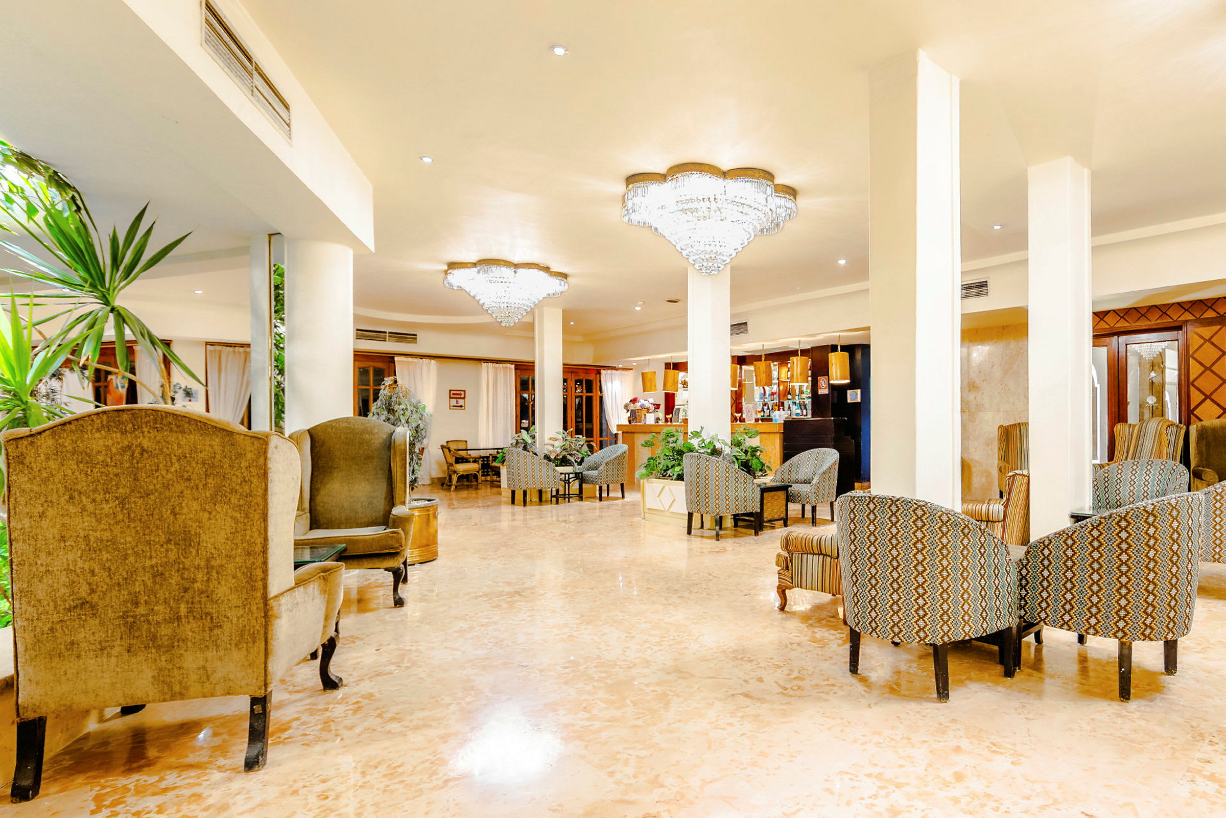 En hotellobby med sittgrupper, gröna växter och kristallkronor i taket. (AI-genererad text)