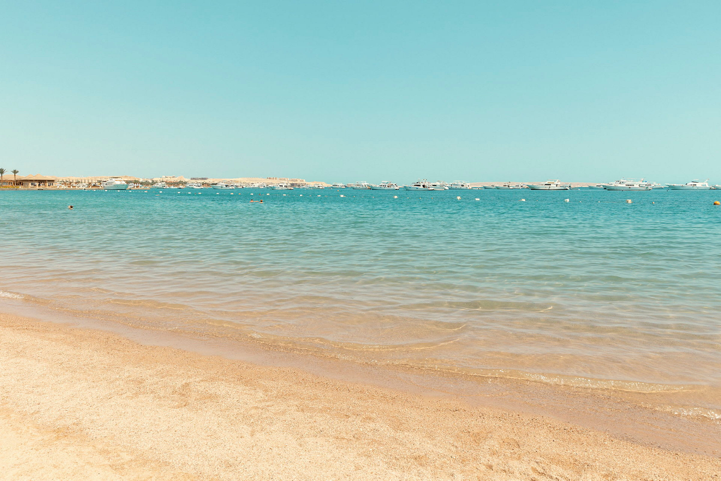 En sandstrand med klart, blått vatten och båtar i fjärran. (AI-genererad text)