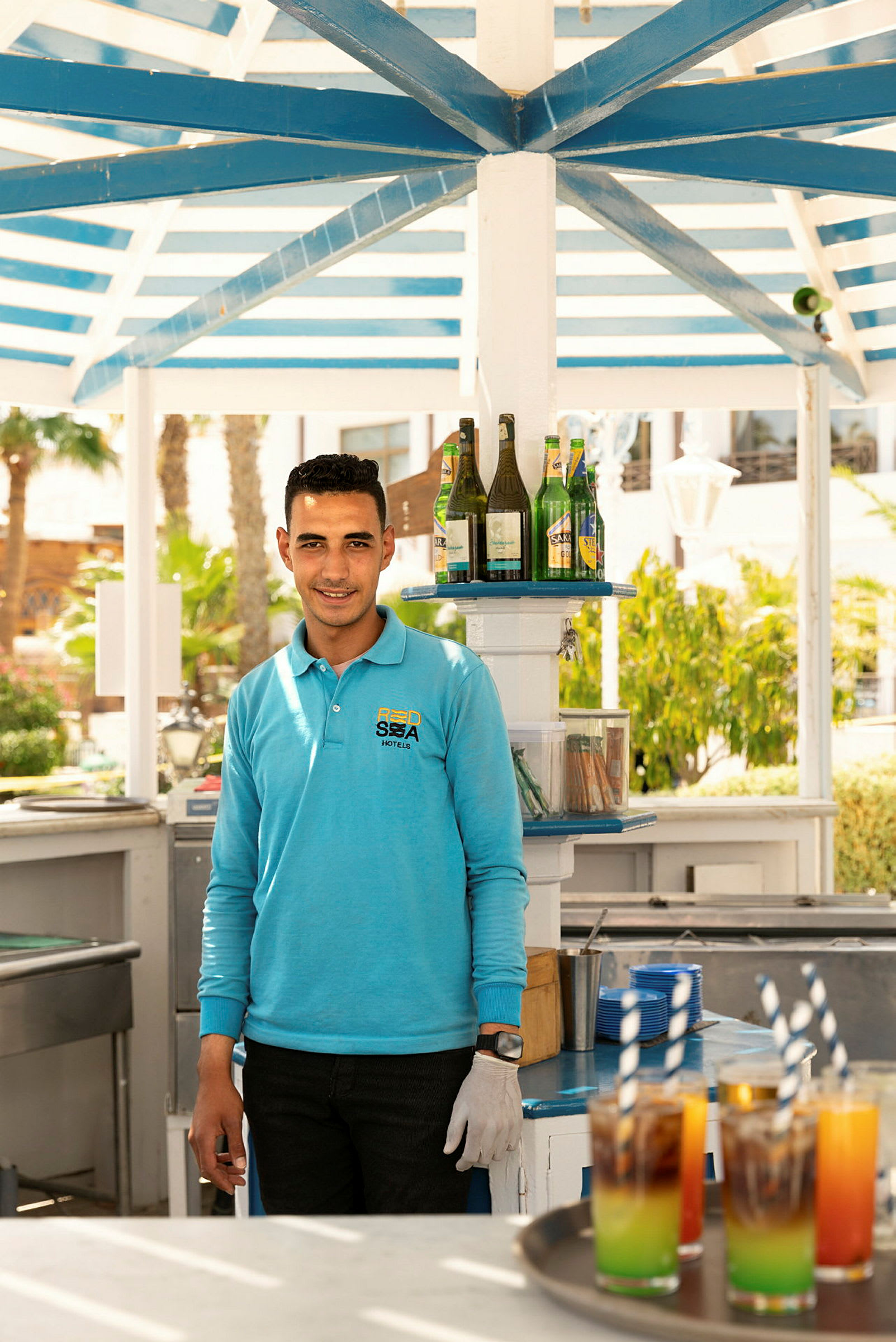 En drinkstation under ett skärmtak, med färgglada drycker och flaskor på en hylla. (AI-genererad text)