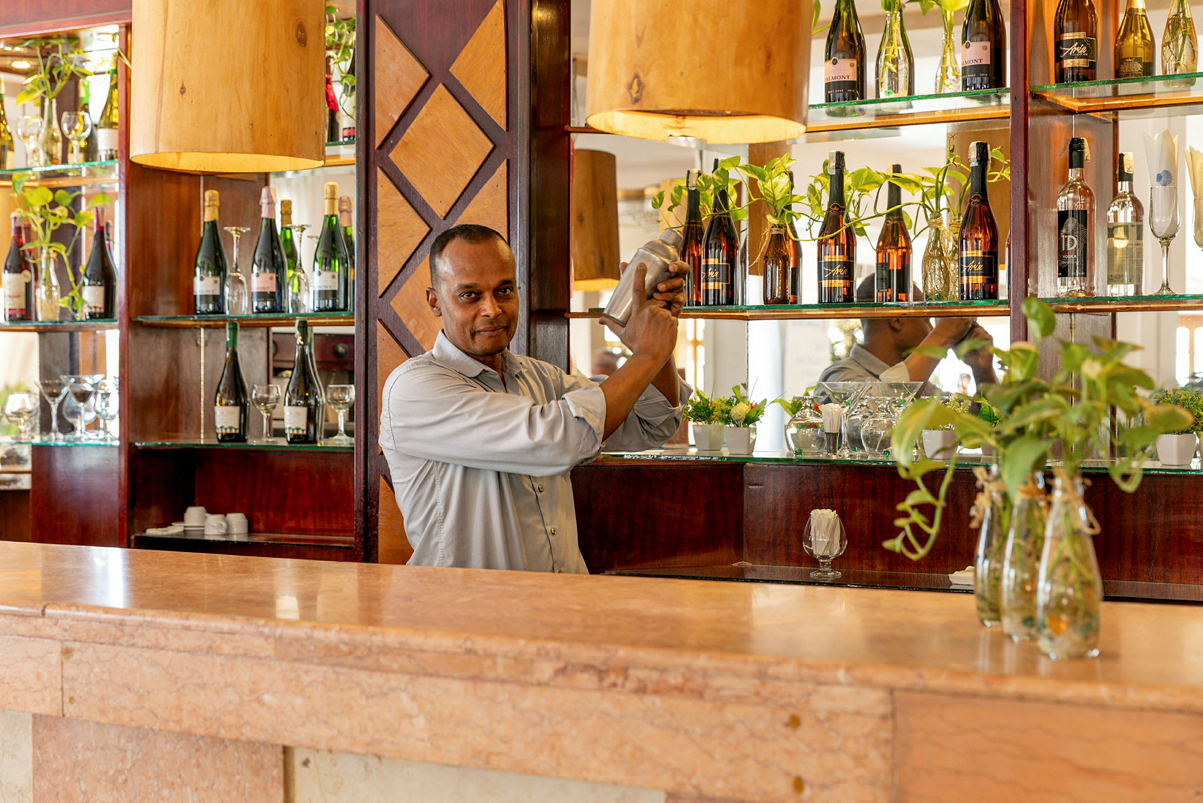 En bartender skakar en cocktail bakom en bardisk med flaskor och dekorationer. (AI-genererad text)