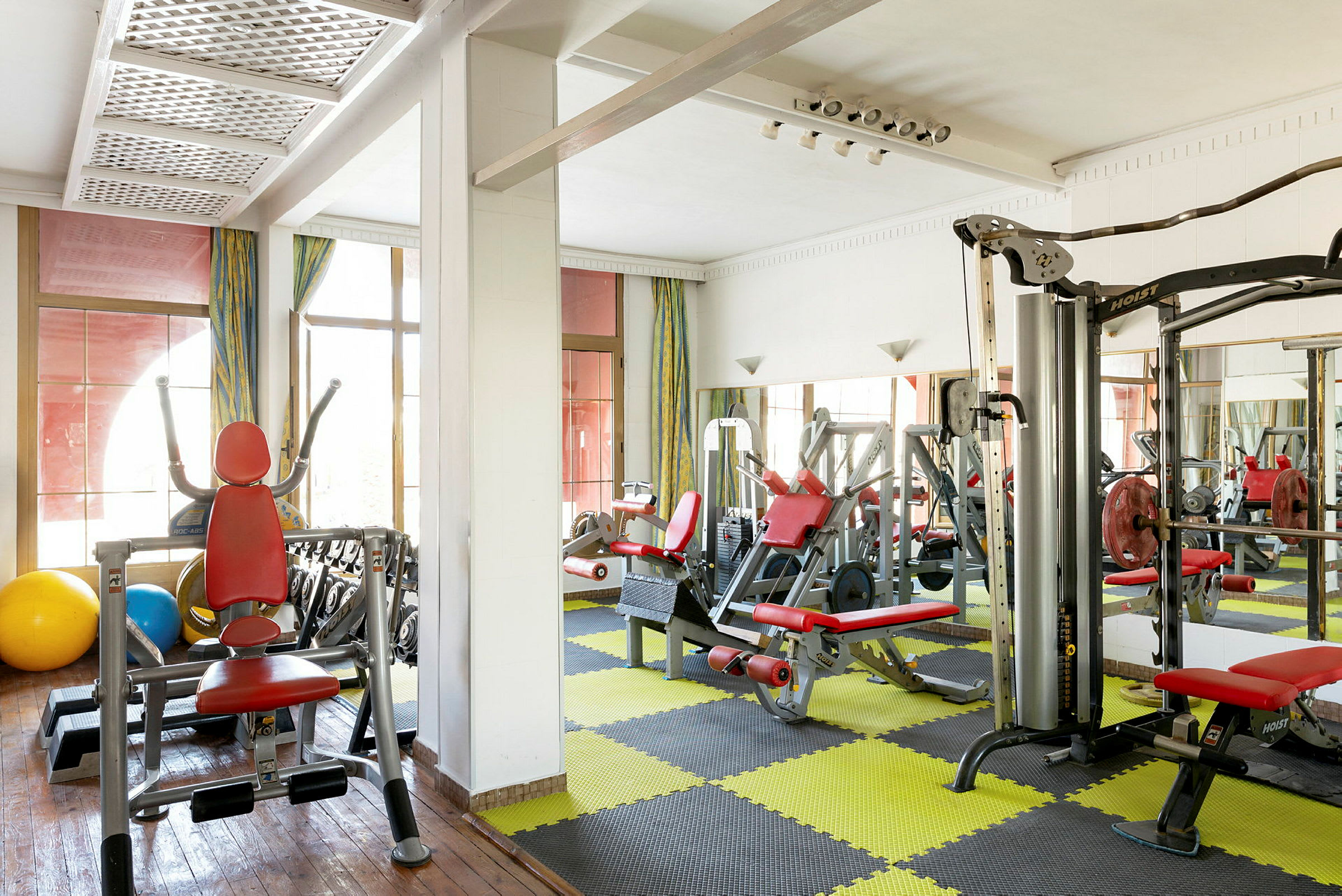 Bild av ett gym med träningsmaskiner och gulsvart mönstrad golvmatta. (AI-genererad text)