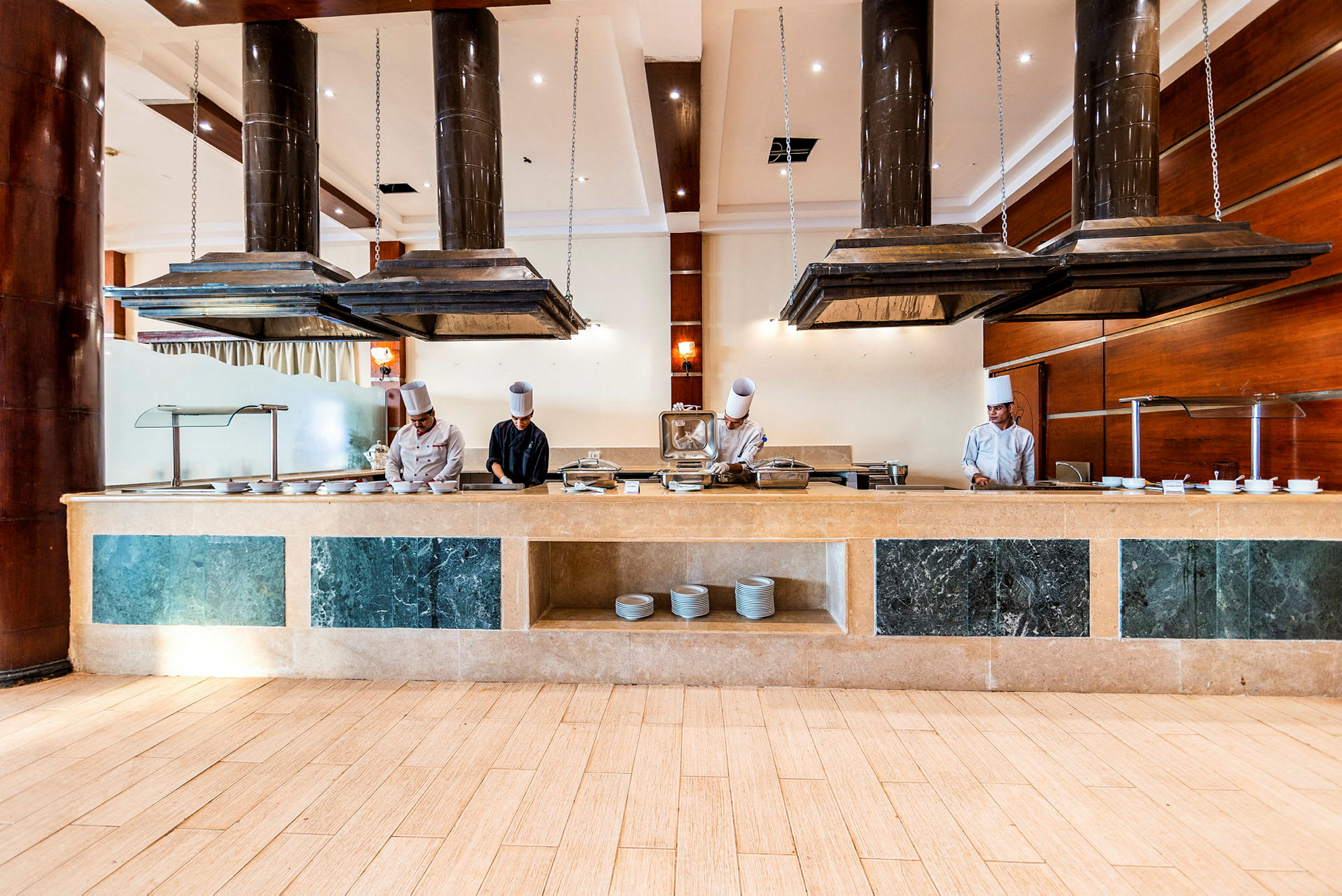 En hotellrestaurang med en buffédisk och köksutrustning under stora köksfläktar. (AI-genererad text)