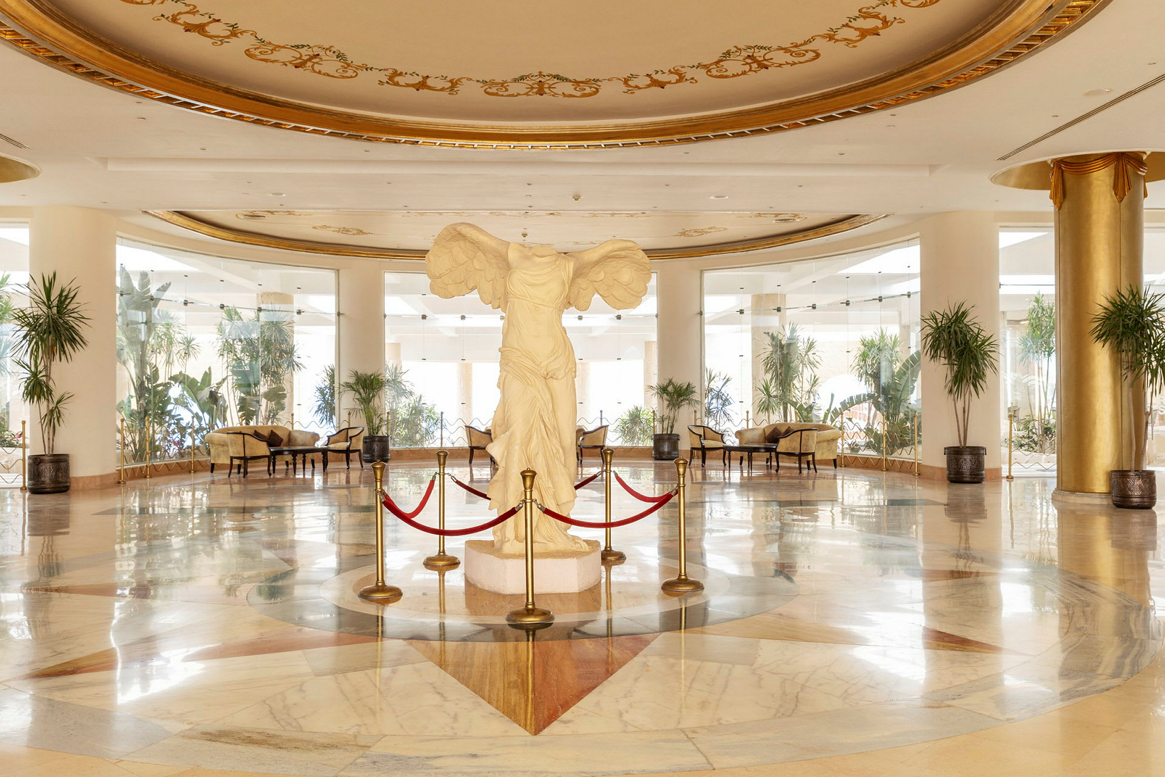 Interiör av en elegant hotellfoajé med en vit staty omgiven av röda rep i centrum. (AI-genererad text)
